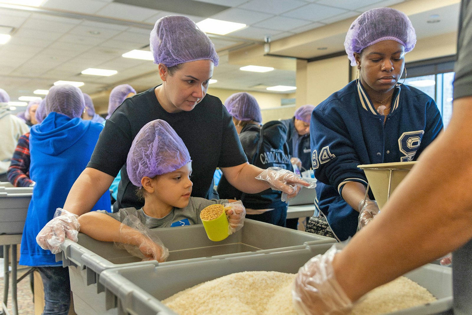 Volunteers fill cups and bags with rice, vitamin-fortified crushed soy, a vitamin blend, and dehydrated vegetables at packaging stations set up in the St. Isidore social hall. The organized effort will allow those who receive the meals to simply add six cups of water to feed up to six adults or 12 children.