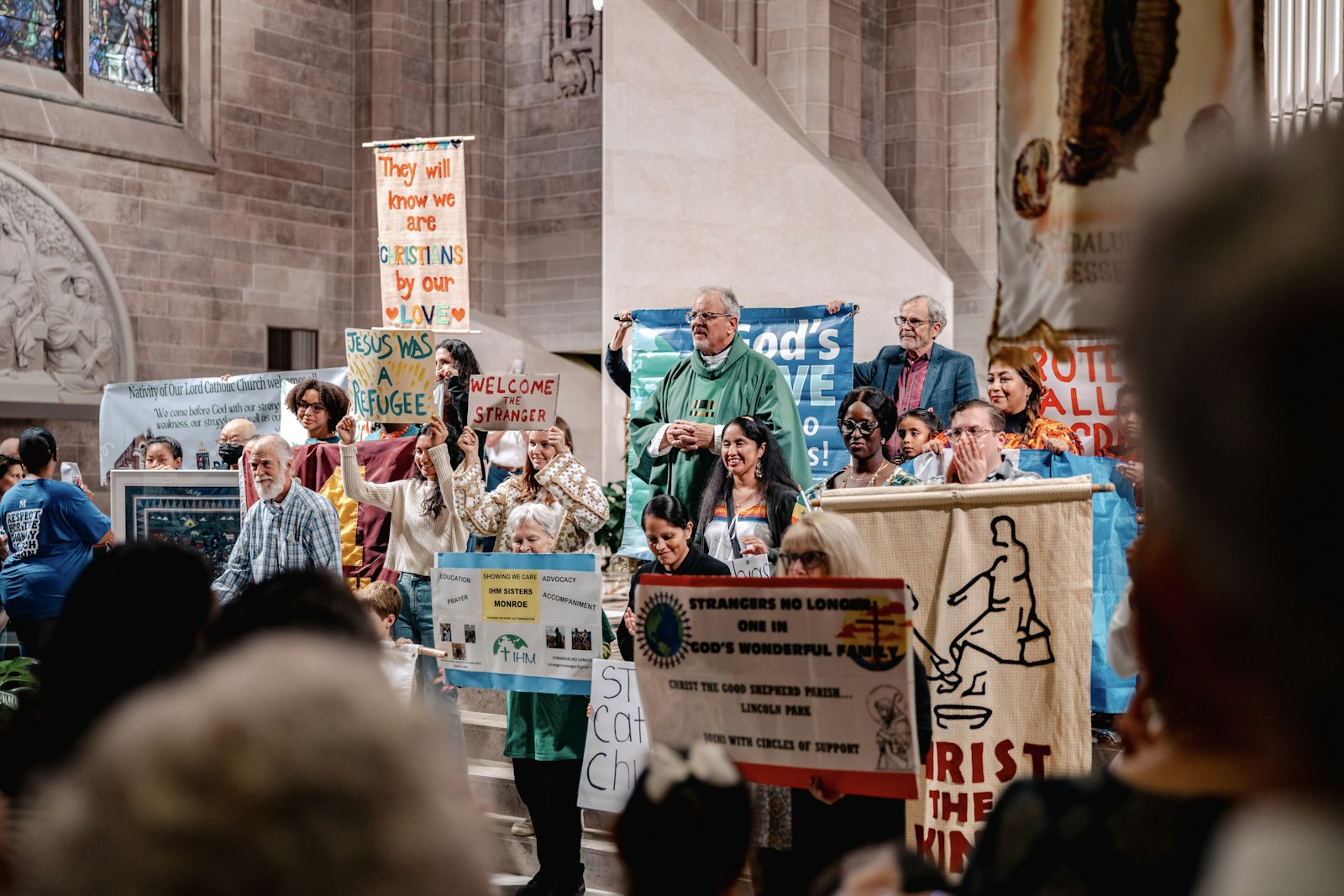 El P. David Buersmeyer, capellán de Strangers No Longer, permanece de pie entre jóvenes que sostienen pancartas y carteles en apoyo de los inmigrantes y refugiados antes de la misa en la Cathedral of the Most Blessed Sacrament.