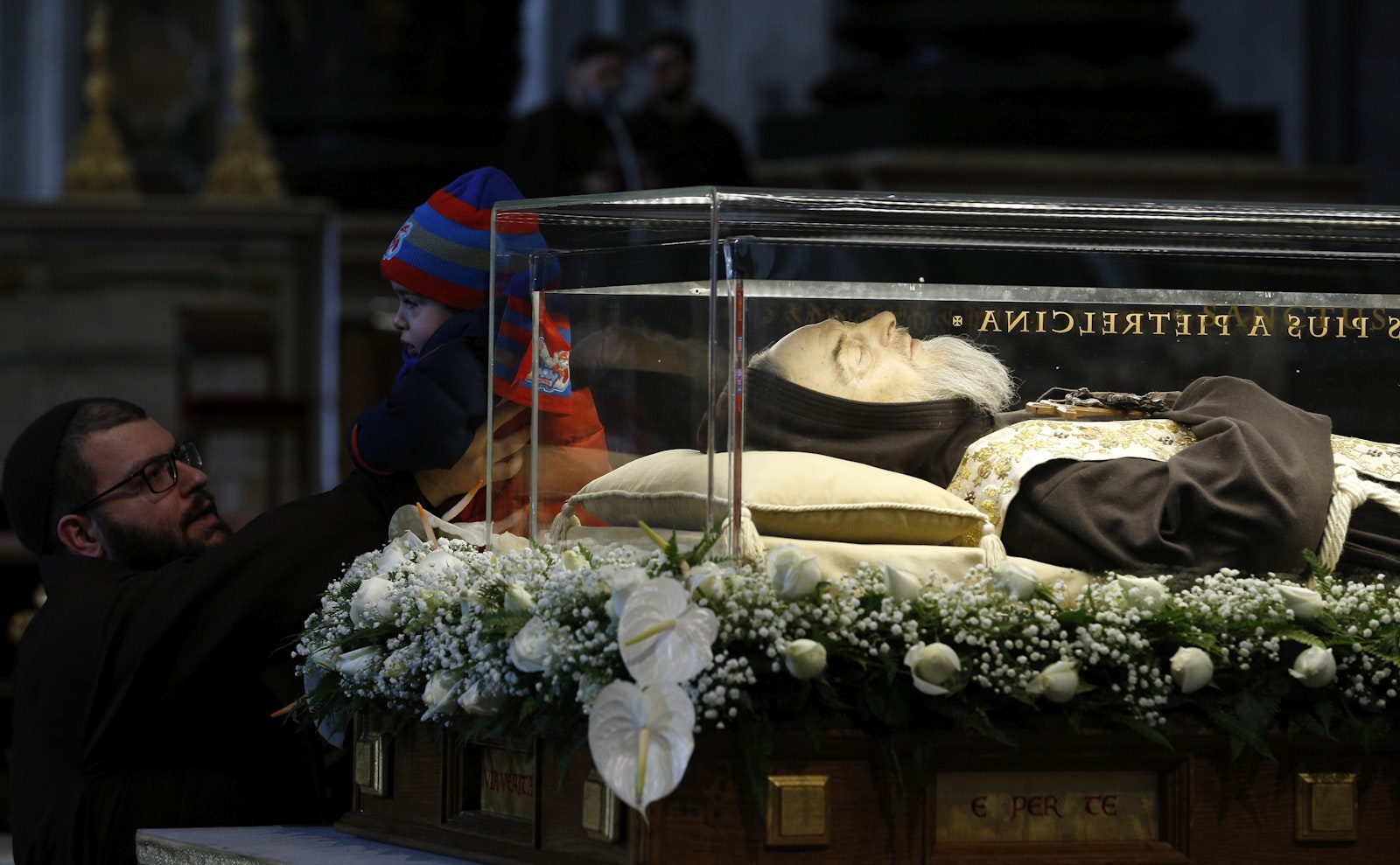 A child is lifted to come into contact with the glass case containing the body of St. Padre Pio in St. Peter's Basilica at the Vatican Feb. 6. The bodies of St. Padre Pio and St. Leopold Mandic were brought to Rome at the request of Pope Francis for the Year of Mercy. (CNS photo/Paul Haring)