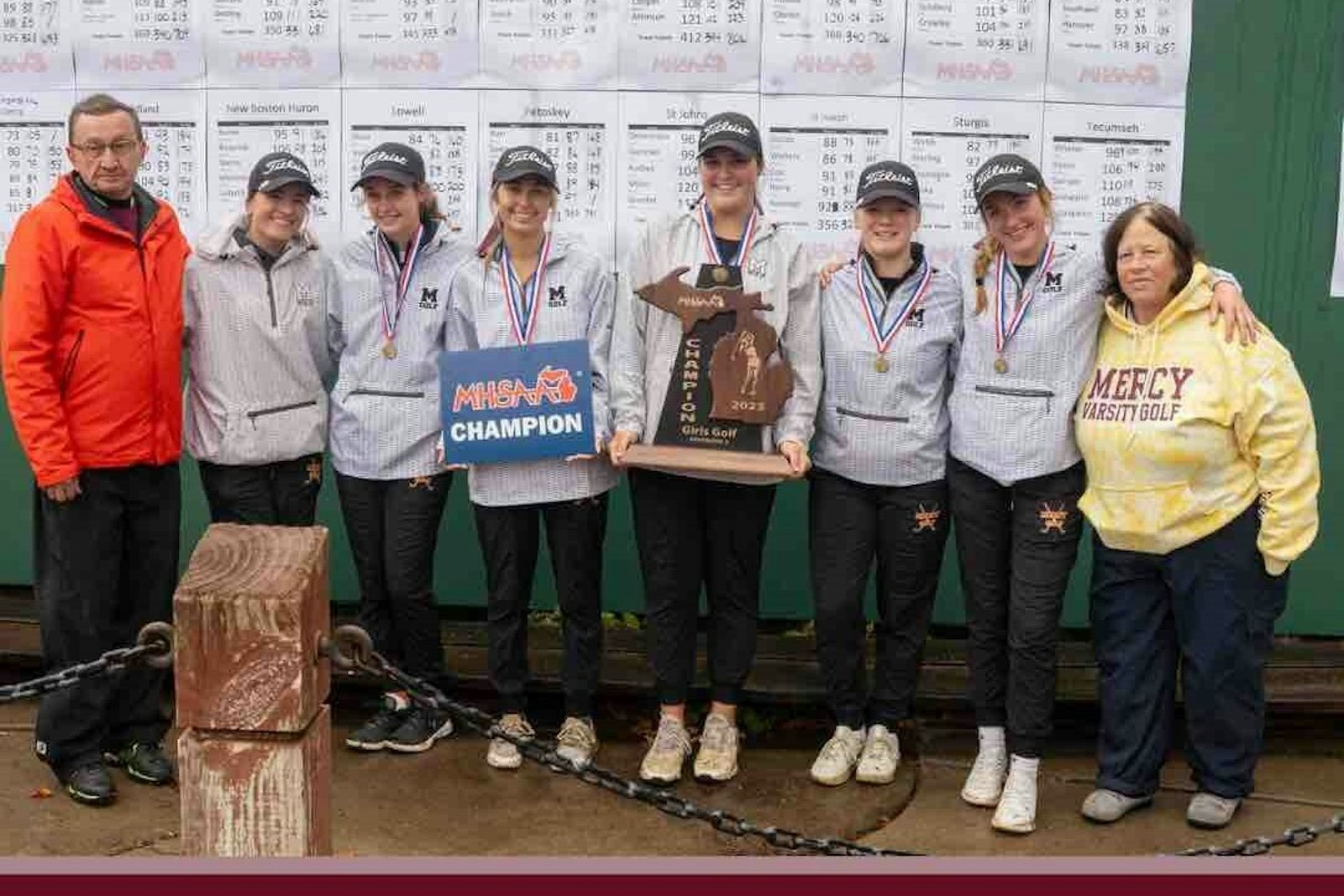 Mercy’s repeat MHSAA Division 2 girls golf champions: Assistant coach Rich Mardeusz, junior Rayna Salazar, junior Marie Schueneman, senior Brinlee Nay, senior Abby Slankster, junior Macy Morphew, junior Lila Polakowski, coach Vicky Kowalski. Missing is junior Maeve Casey because after scoring 73 on Friday she got on a plane to play AAA hockey in Minnesota. (Photo courtesy of Mercy Athletic Department)