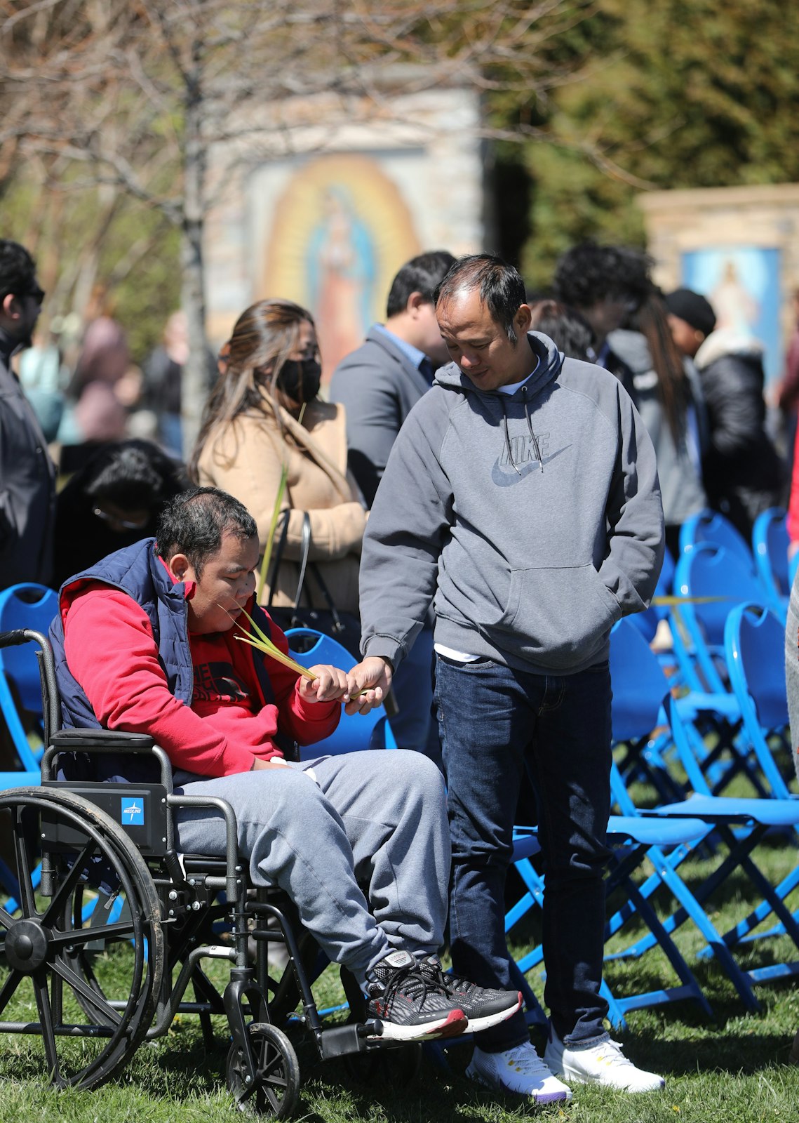 A man helps a family member in a wheelchair during Palm Sunday Mass outside St. Mary's Chapel at the National Shrine Grotto of Our Lady of Lourdes in Emmitsburg, Md. (OSV News photo/Bob Roller)