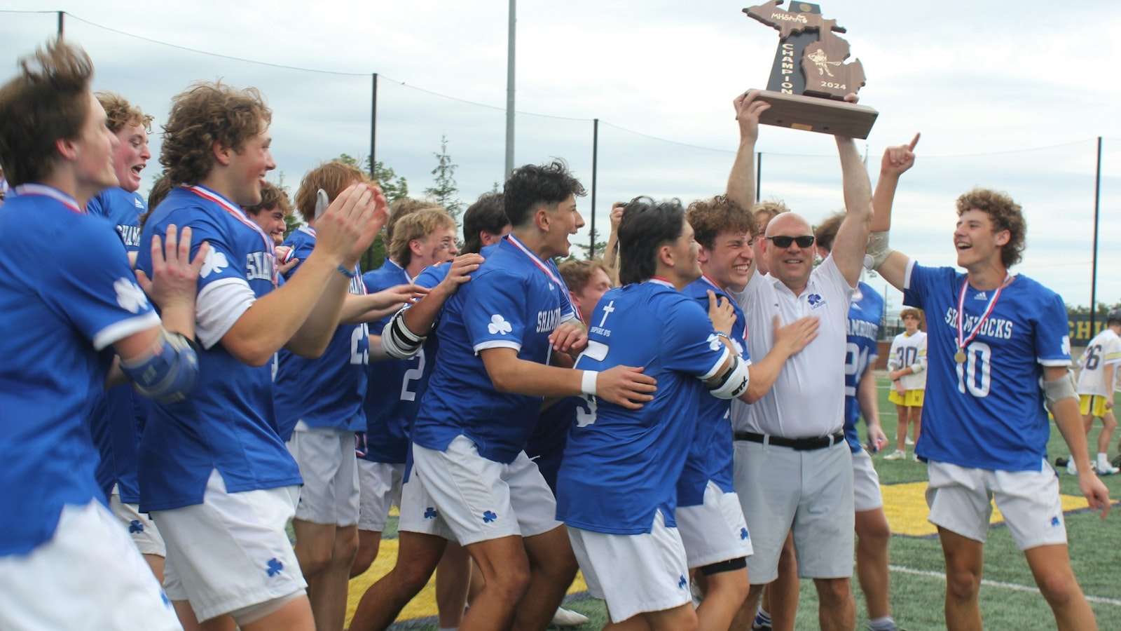 Catholic Central lacrosse players celebrate as coach Dave Wilson hoists the MHSAA Division 1 state championship trophy. The Shamrocks won the state title with a 14-8 come-from-behind victory over Hartland. (Photo by Wright Wilson | Special to Detroit Catholic)