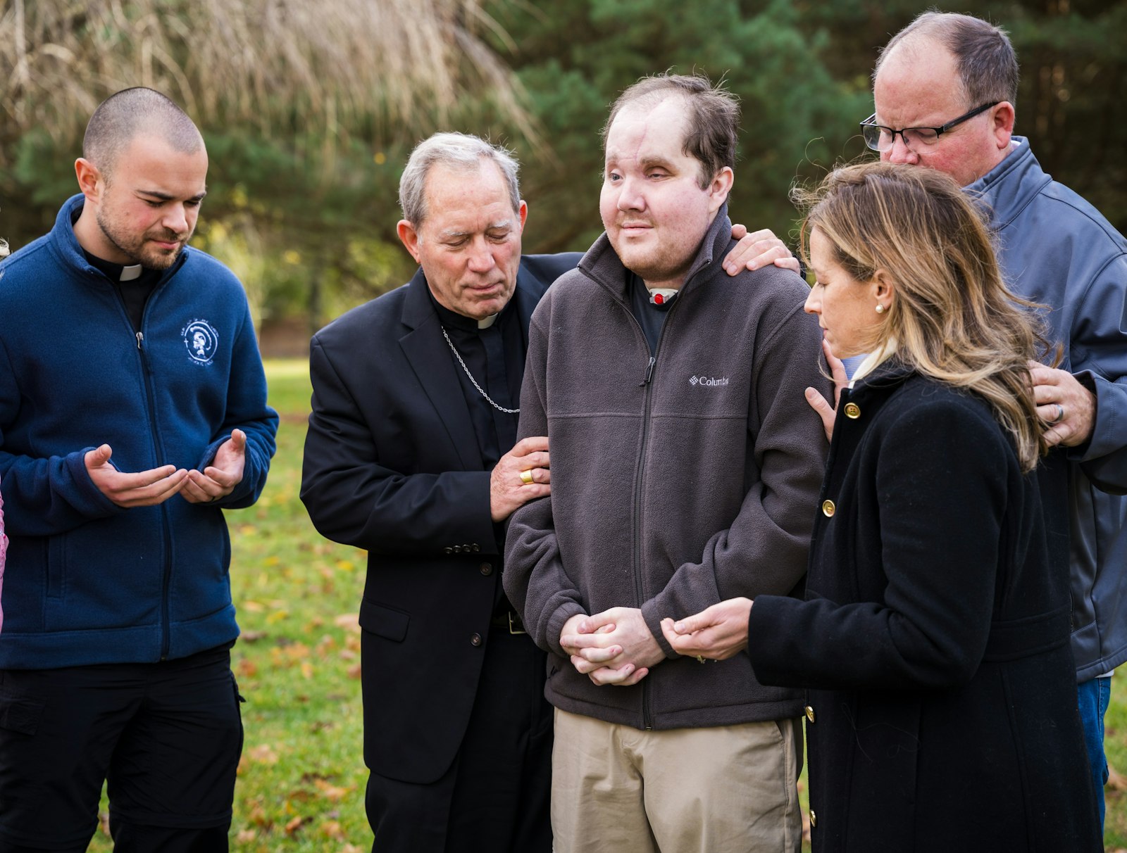 Bishop Robert D. Gruss of Saginaw, Mich., prays with face transplant recipient Derek Pfaff, a parishioner in the Diocese of Saginaw, at his family home in Harbor Beach Nov. 23, 2024. Derek's face transplant is the second one done by the Mayo Clinic in Rochester, Minn. Also pictured are Father Kevin Wojciechowski, Erin Looby Carlson and Jerry Pfaff, Derek's father. (OSV News photo/Chris Gildenstern, courtesy BCD)