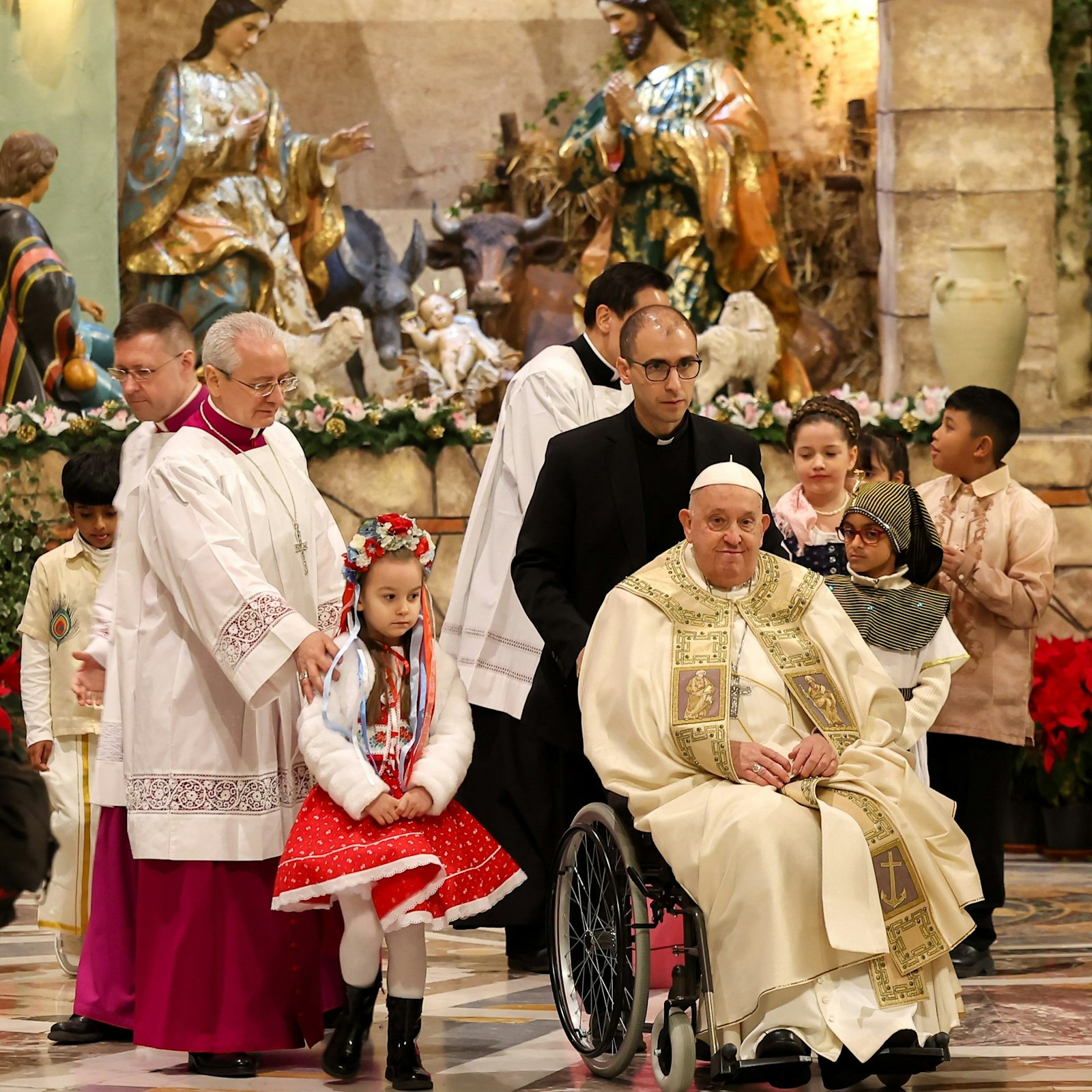 Pope Francis, accompanied by children in traditional attire, smiles after delivering a statue of the baby Jesus to the Nativity scene in St. Peter's Basilica at the end of the Christmas Mass at Night Dec. 24, 2024. (CNS photo/Lola Gomez)