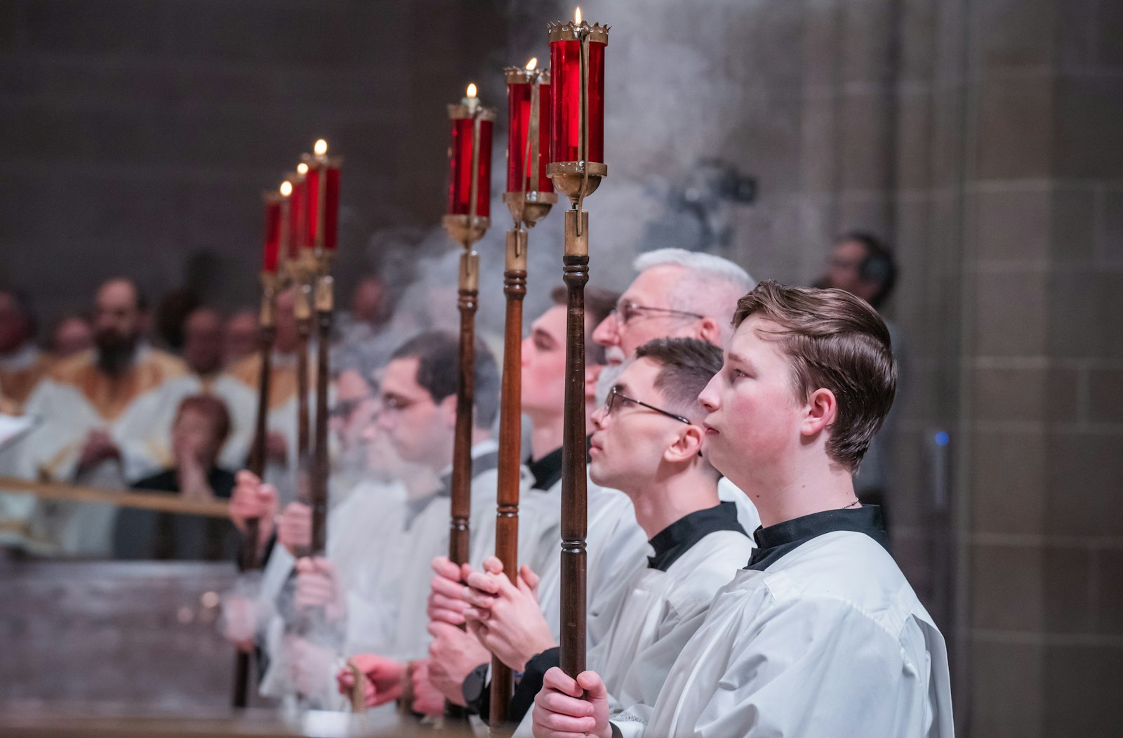 Altar servers hold candles as incense billows during the Chrism Mass.