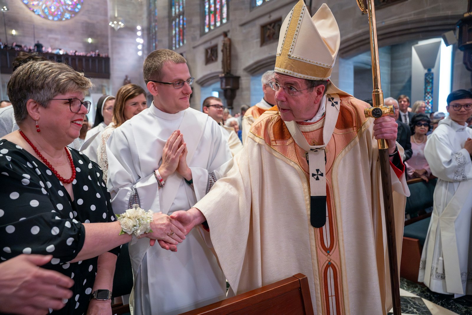 Archbishop Vigneron shakes the hand of Kris Kurt, the mother of Fr. Matthew Kurt, middle, as he processes into the cathedral before the ordination rite.