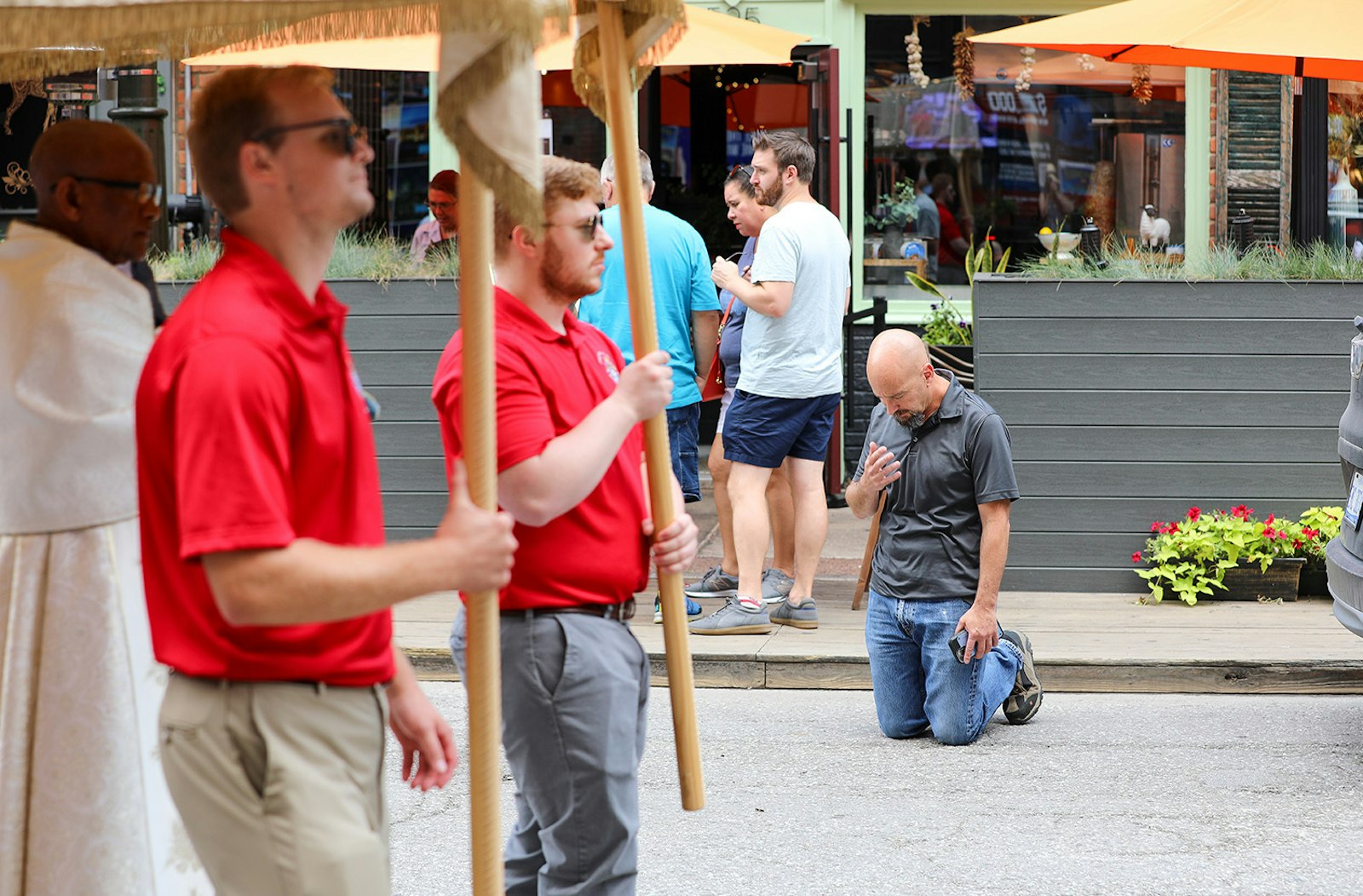 Um homem se ajoelha e para para adorar enquanto um demônio carregando Jesus passa no Santíssimo Sacramento durante uma procissão por Greektown em 23 de julho.