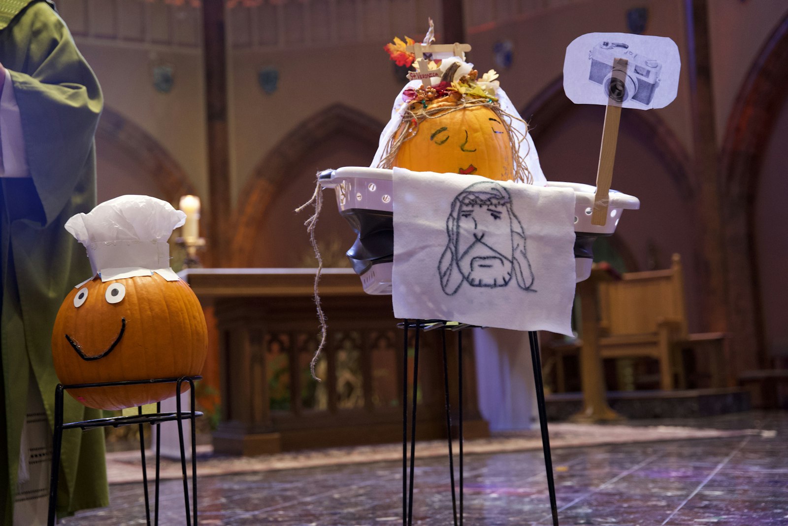 La calabaza de Santa Verónica de los alumnos de quinto grado, no solo incluía su velo con el rostro de Jesús, sino también un cesto de ropa y una cámara, lo que representa que ella es la patrona de los trabajadores de la lavandería y la fotografía. A la izquierda está Santa Marta, representada como cocinera porque es la santa patrona de los cocineros.