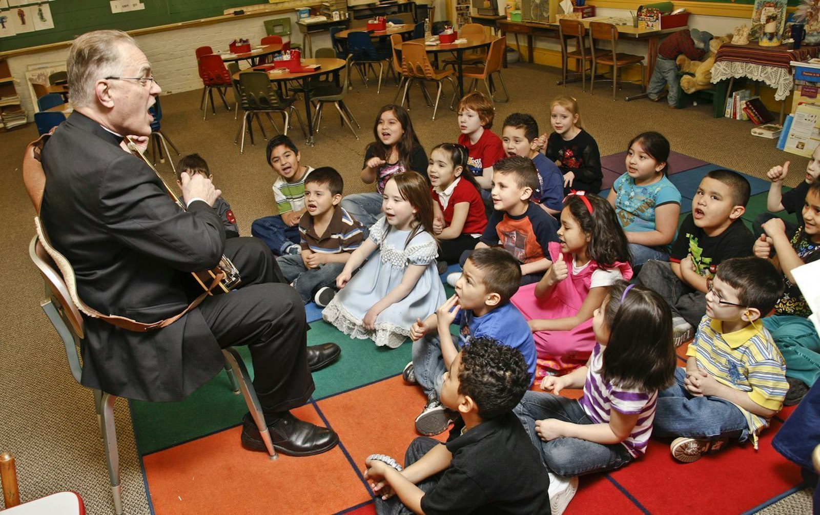 Then-Msgr. Hanchon strums his ukulele as he sings to a group of schoolchildren at Holy Redeemer School in southwest Detroit. (Larry A. Peplin | Detroit Catholic file photo)