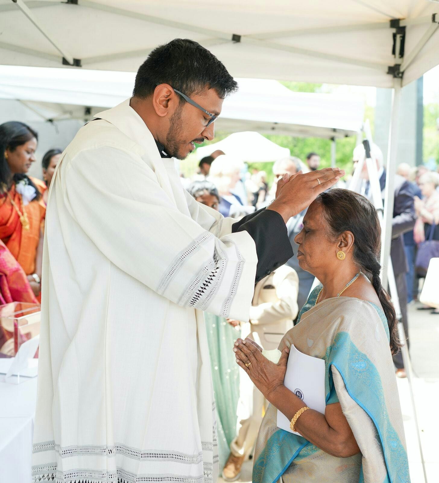El padre Michael Selvaraj bendice a su madre, quien hizo un viaje desde su hogar en India para acompañarlo en la catedral después de su ordenación sacerdotal el 27 de mayo.
