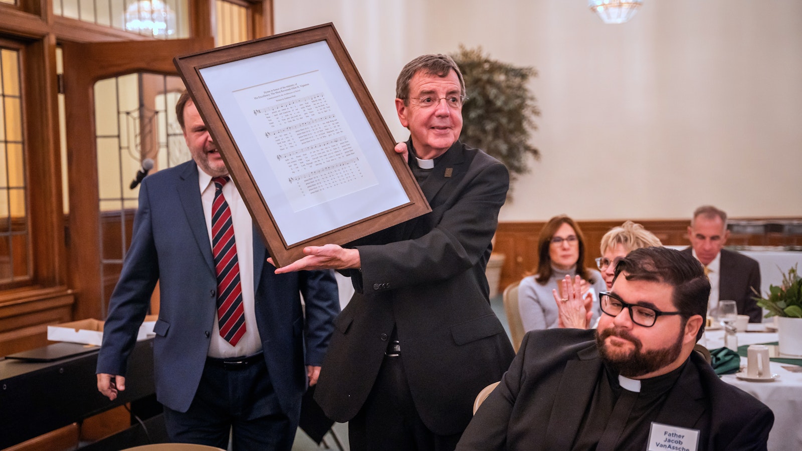 Archbishop Vigneron holds up a framed copy of a hymn written in his honor given to him as a gift Oct. 16, 2023, during a celebration of his 75th birthday. (Valaurian Waller | Detroit Catholic)