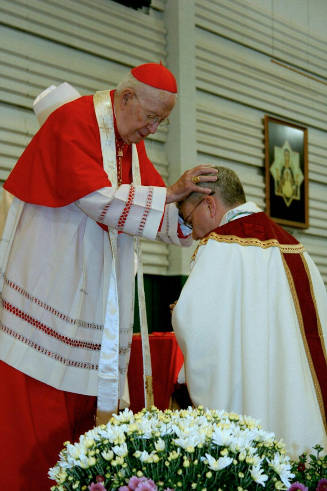 El Cardenal Edmund C. Szoka (Q.E.P.D.), arzobispo de Detroit en la década de 1980, impone sus manos sobre la cabeza del Obispo Monforton durante su Misa de consagración episcopal el 10 de septiembre de 2012, en la Franciscan University en Steubenville, Ohio.