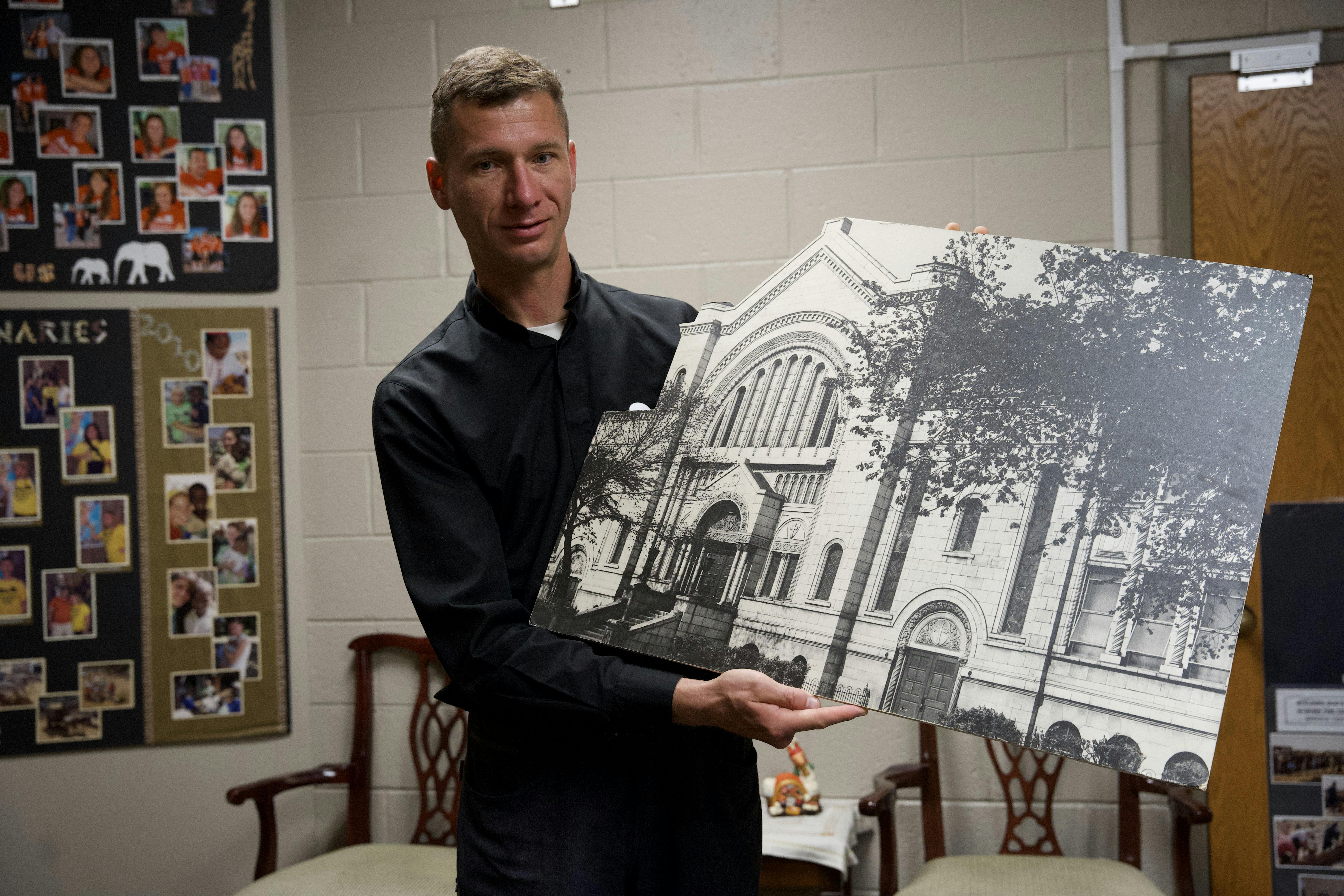 Fr. Malek holds a cutout image of the second brick church. Many of his current parishioners attended this church before the parish moved to current building in 1988, and still talk about how beautiful it was.