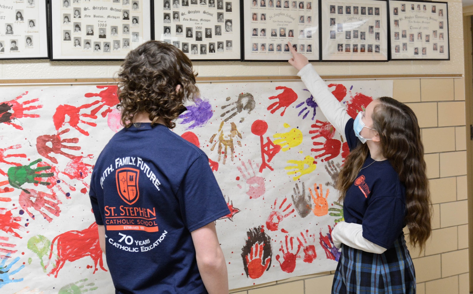 Students point to former St. Stephen School classes as they paint a banner with handprints in the school's hallway.