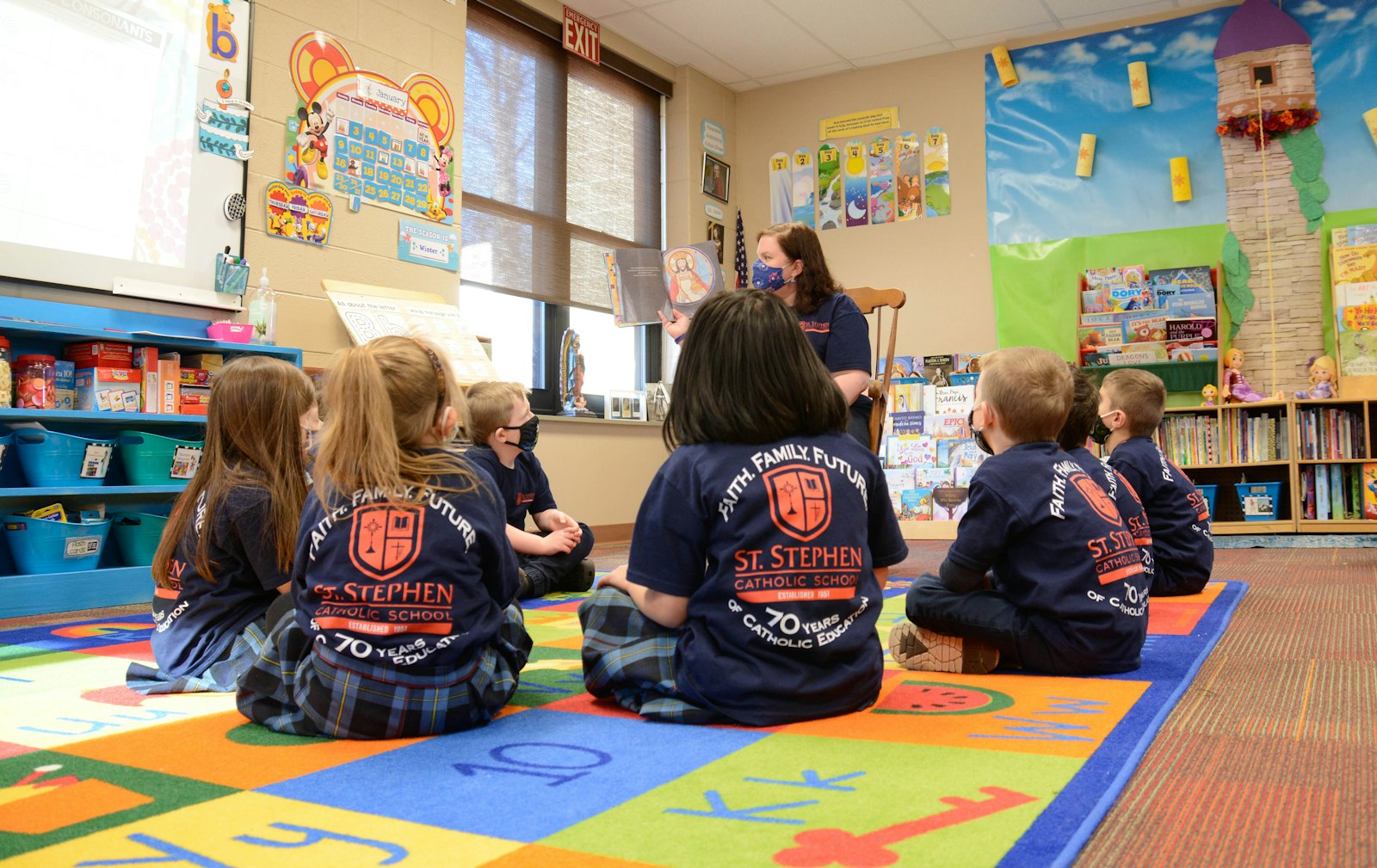 Los alumnos de St. Stephen escuchan un cuento leído por su profesora mientras llevan camisetas con el logotipo y el lema del colegio. Muchas familias de la escuela son multigeneracionales, dicen los responsables de la escuela.