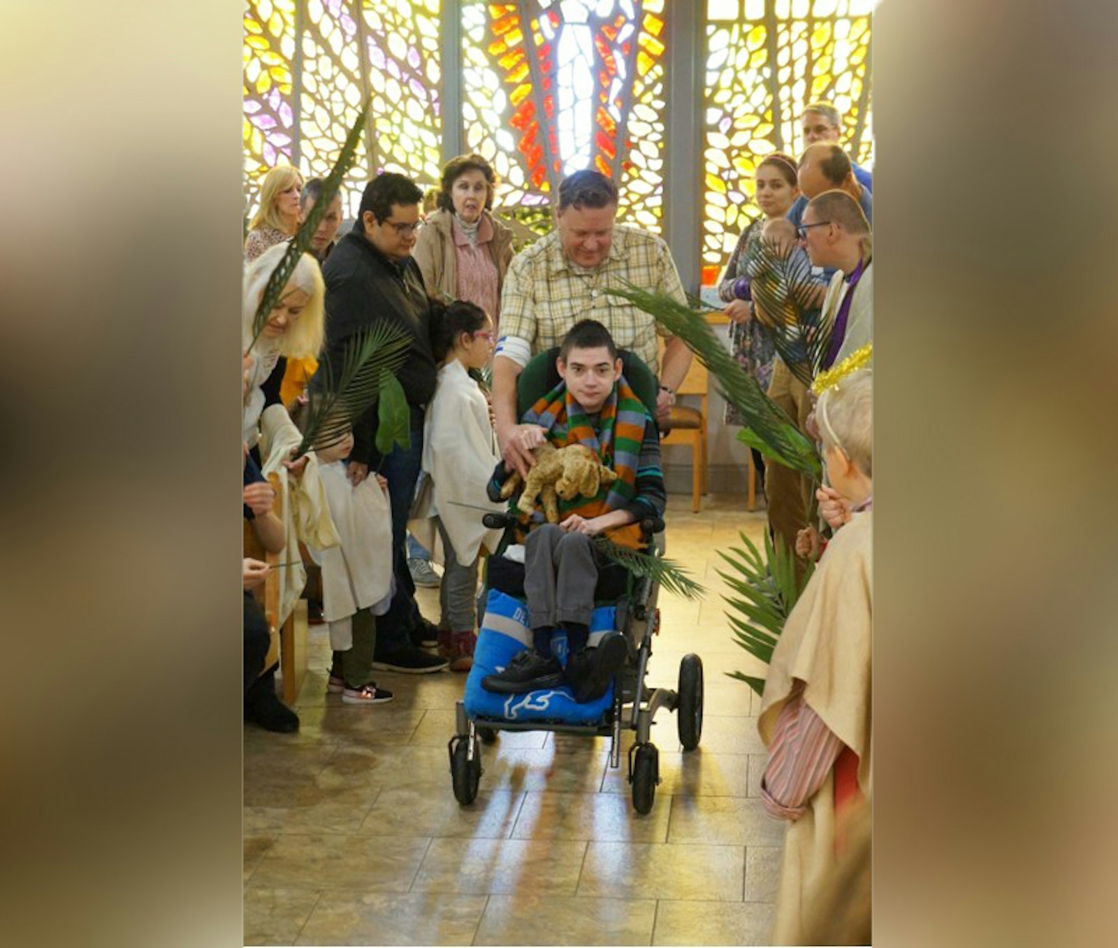 Cameron Brunt, en el papel de Jesús, entra en Jerusalén llevando un burro de peluche mientras el catequista George Downey lo lleva por el pasillo, bordeado por participantes del programa de necesidades especiales y cuidadores, en una recreación de la lectura del Evangelio del Domingo de Ramos.