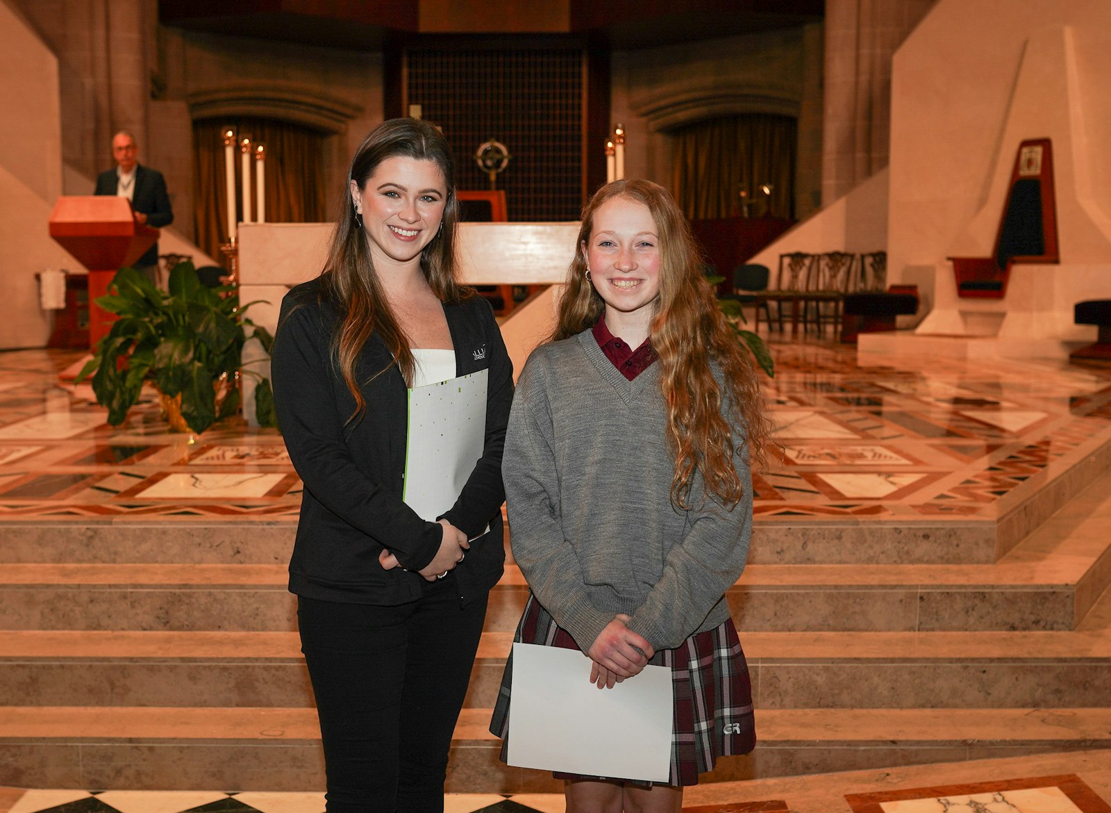 Genevieve Campbell, right, a freshman at Gabriel Richard High School in Riverview, receives her first-place award from Jessica Rabine, communications coordinator for Alliance Catholic Credit Union. Campbell's winning apparel design depicted the Holy Trinity, with different levels of fire representing different characteristics of the Divine Persons of the Trinity.