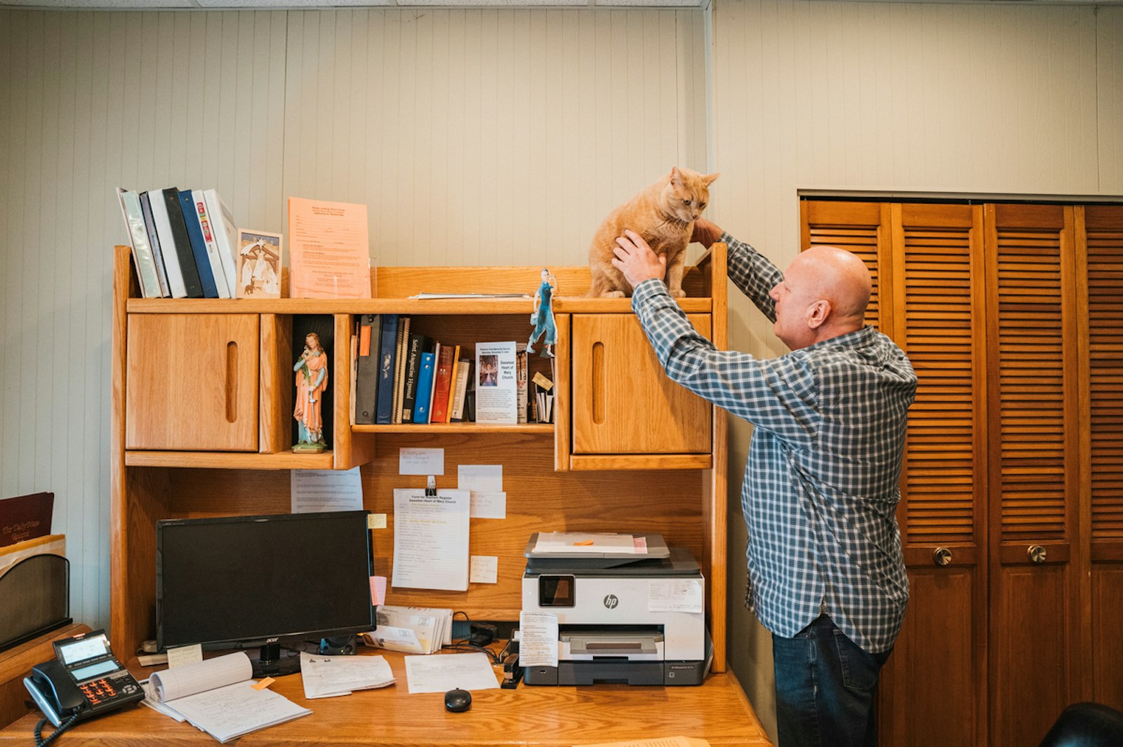 Rick Jakacki retrieves Casey from one of his favorite napping spots: on top of Fr. Greg Tokarski's desk in the rectory office at Sweetest Heart of Mary.