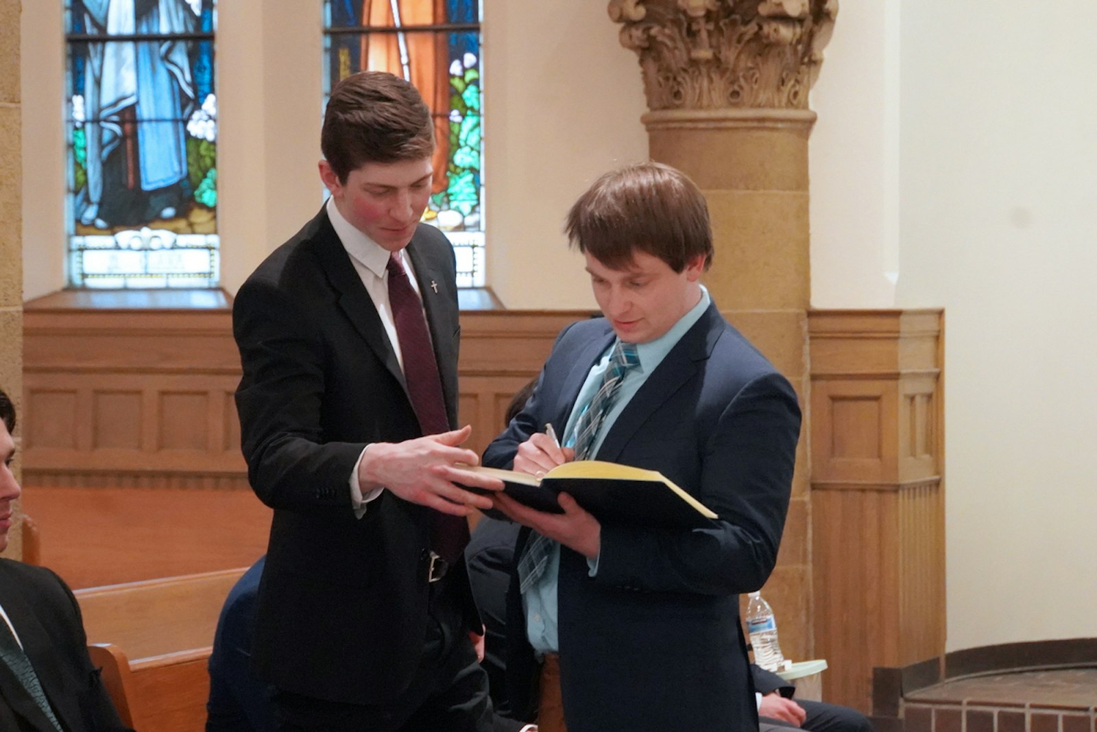 New grand knight Shaun McGrath holds the registry of the founding members of the Blessed Carlo Acutis Knights of Columbus Council as a newly enrolled third-degree knight signs his name. McGrath said the young men at Detroit Catholic Campus Ministry were looking for a more formal structure to encourage fellowship and service among men on campus.