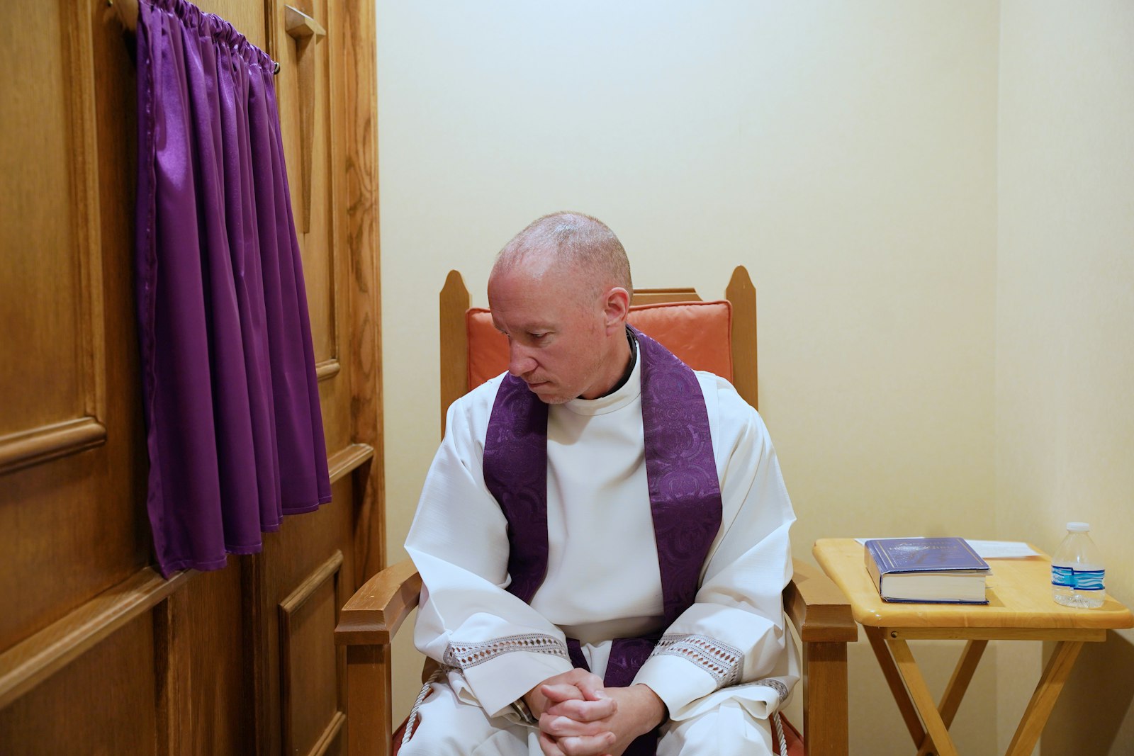 Fr. Andrew Dawson sits next to the new confessional screen at Prince of Peace Parish in West Bloomfield in this staged photo.