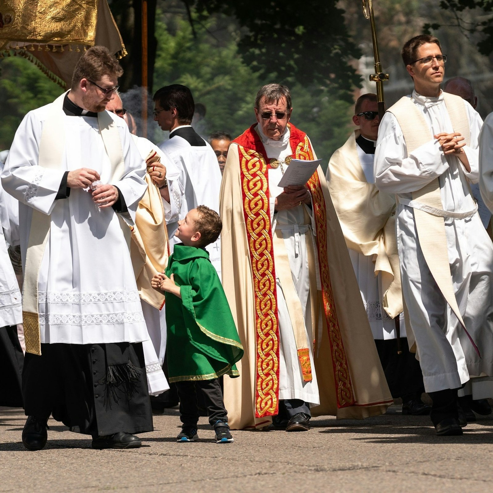 Five-year-old Lucas Mattos gets the attention of Fr. David Tomaszycki, left, as he marches at the front of the Eucharistic procession alongside Archbishop Allen H. Vigneron. Mattos wore his own priestly "vestments," a gift from his grandparents. Lucas' mother said the boy has shown an interest in the Eucharist from a young age. (Melanie Reyes | Special to Detroit Catholic)