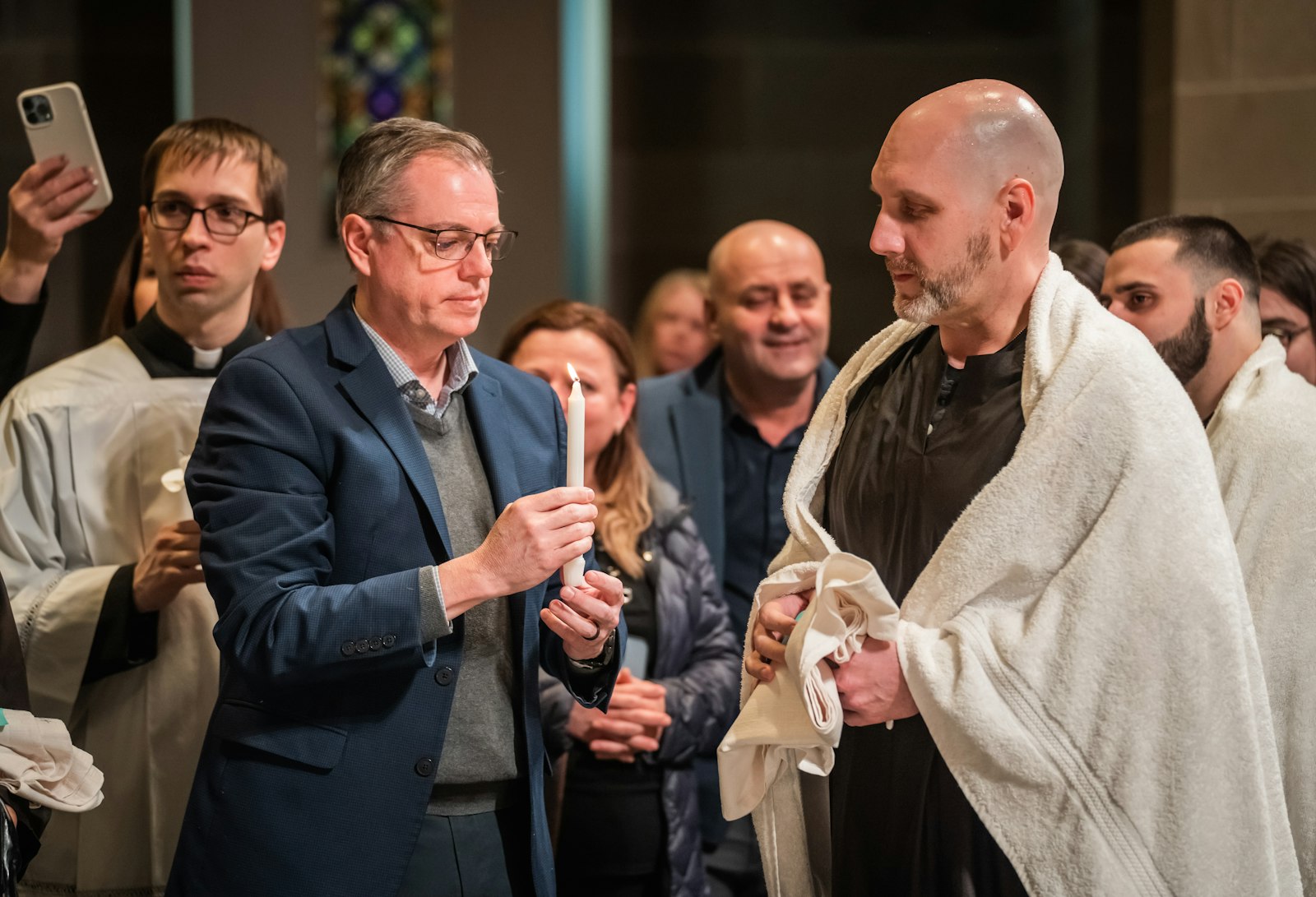 Brian Mull receives the "light of Christ" from his sponsor and co-worker, Jerry McElhone, left, after his baptism. Mull said it was special to enter the Catholic faith alongside his co-workers, receiving baptism, confirmation and first Communion from his boss, Archbishop Vigneron.