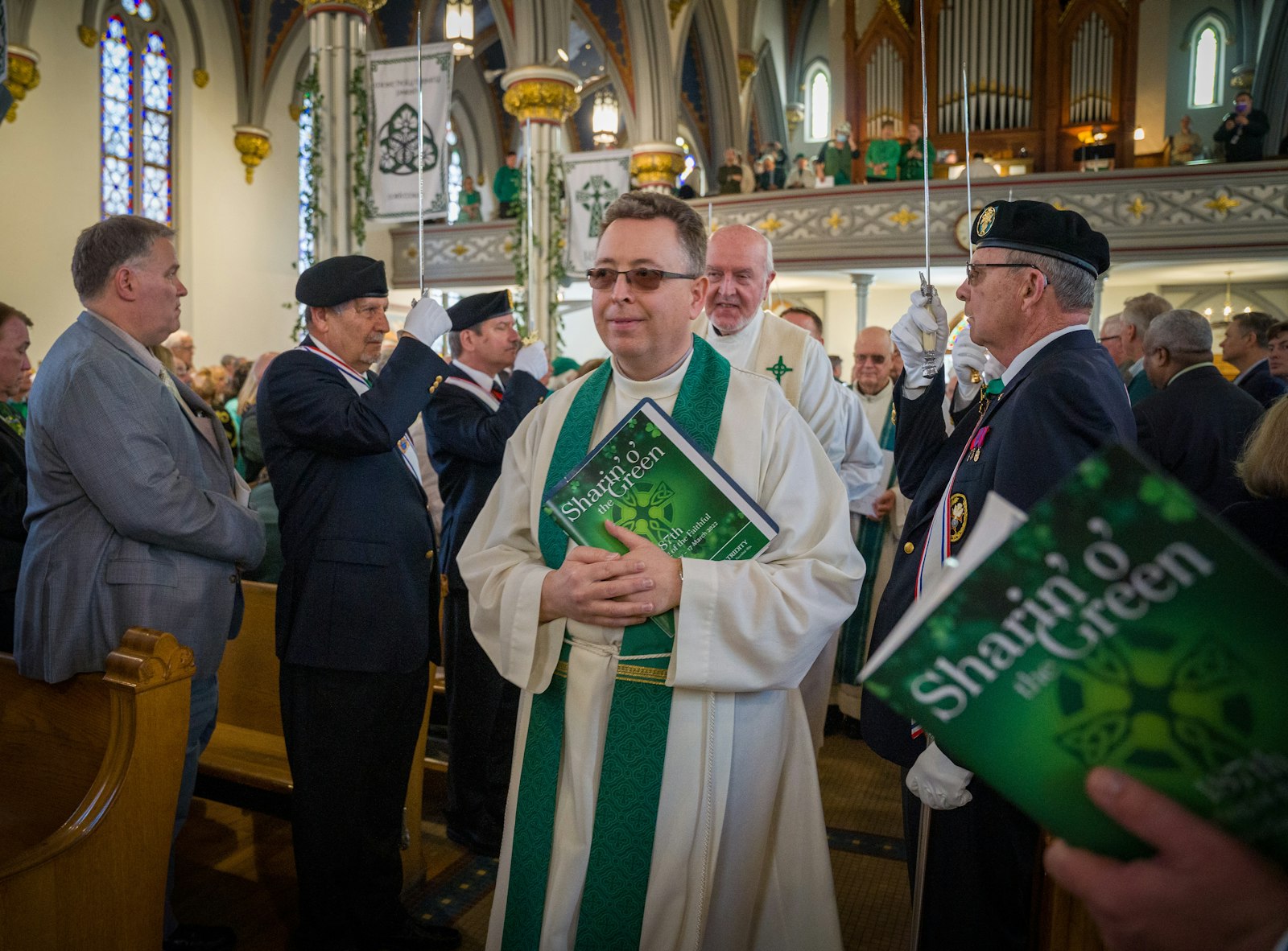 Fr. Brendan McCarrick, SAC, pastor of St. Vincent Pallotti Parish in Wyandotte, holds a "Sharin' o' the Green" Mass booklet as he processes into the church, flanked by members of the Knights of Columbus honor guard.