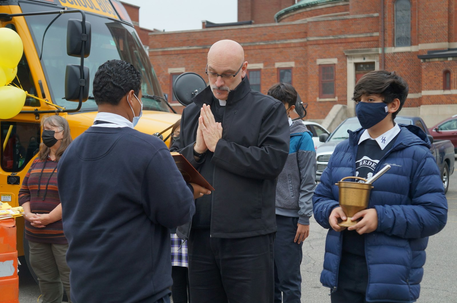 Fr. Dennis Walsh, SOLT, pastor of Holy Redeemer Parish, blesses the new school bus as Holy Redeemer students look on.