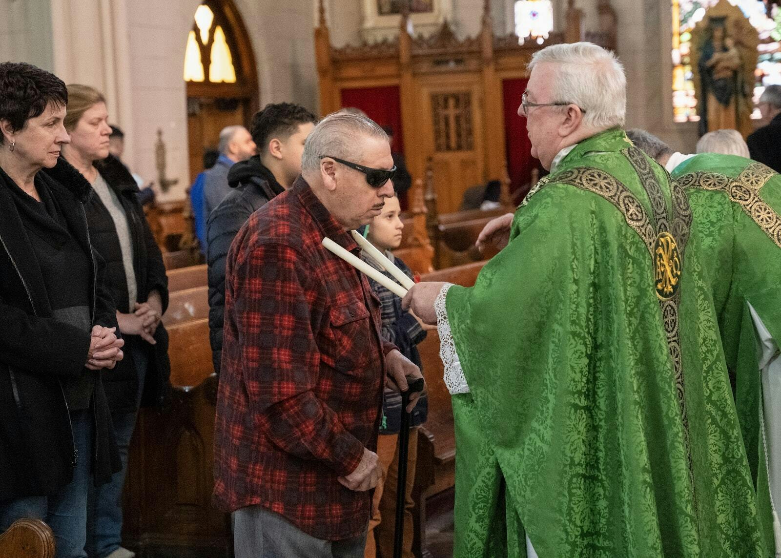 Msgr. Chuck Kosanke, rector of the Basilica of Ste. Anne, blesses parishioners' throats with candles according to the custom of the feast of St. Blaise, invoking the intercession of the fourth-century Armenian bishop and martyr who said that anyone who lit a candle in his memory would be free from infection.