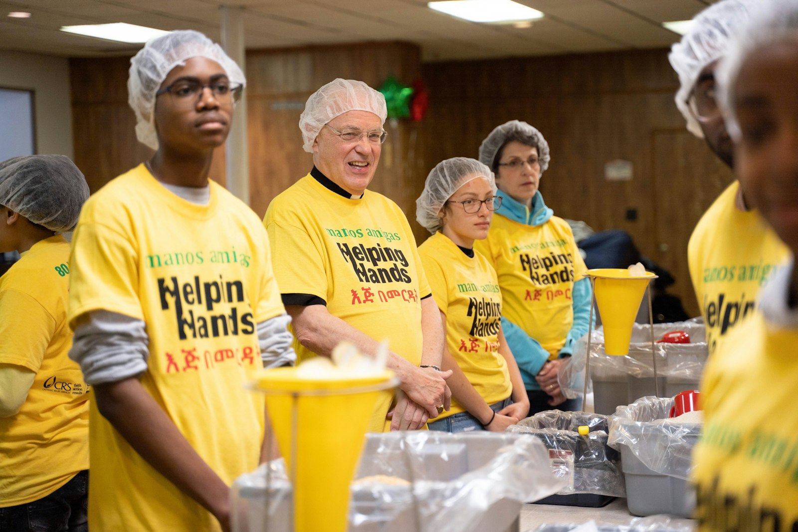 El obispo Hanchon ayuda a los estudiantes a empacar comidas para familias en la pobre nación africana de Burkina Faso el 4 de mayo de 2019 en la parroquia de St. Charles Lwanga en Detroit. En el evento, más de 80 voluntarios empacaron 10,000 comidas para enviar al extranjero, una oportunidad para que los estudiantes de confirmación retribuyan a su familia global, dijo el obispo. (Fotos de Valaurian Waller | Detroit Catholic)