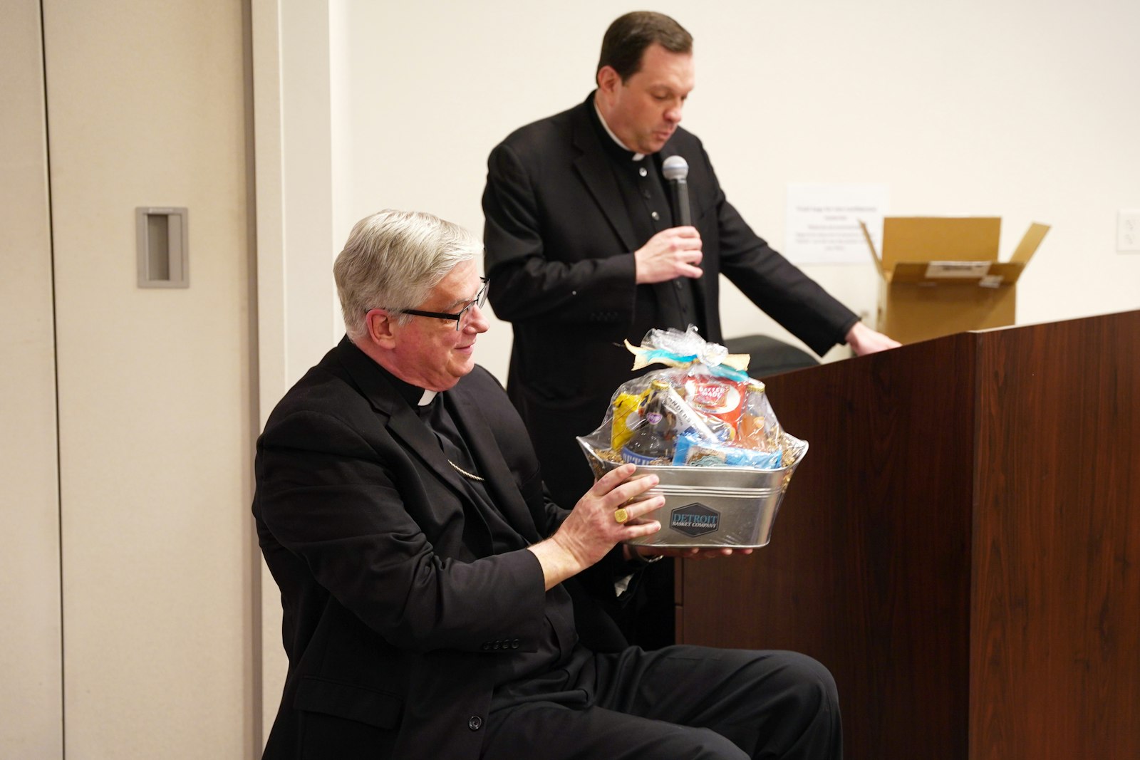 Fr. Jeffrey Day, moderator of the curia for the Archdiocese of Detroit, presents Bishop Battersby with a gift basket filled with Michigan-made products and mementos, a reminder of his roots as he departs for Wisconsin.