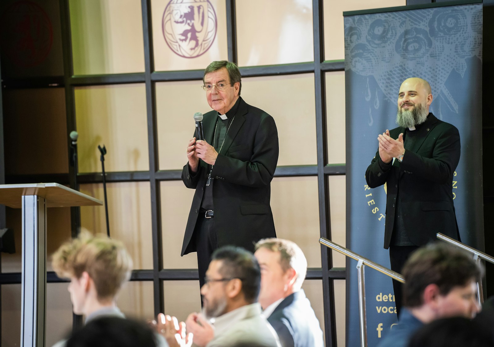 Archbishop Vigneron and Fr. Craig Giera, director of priestly vocations for the Archdiocese of Detroit, right, address the young men gathered in the seminary's gymnasium for dinner and discussion.