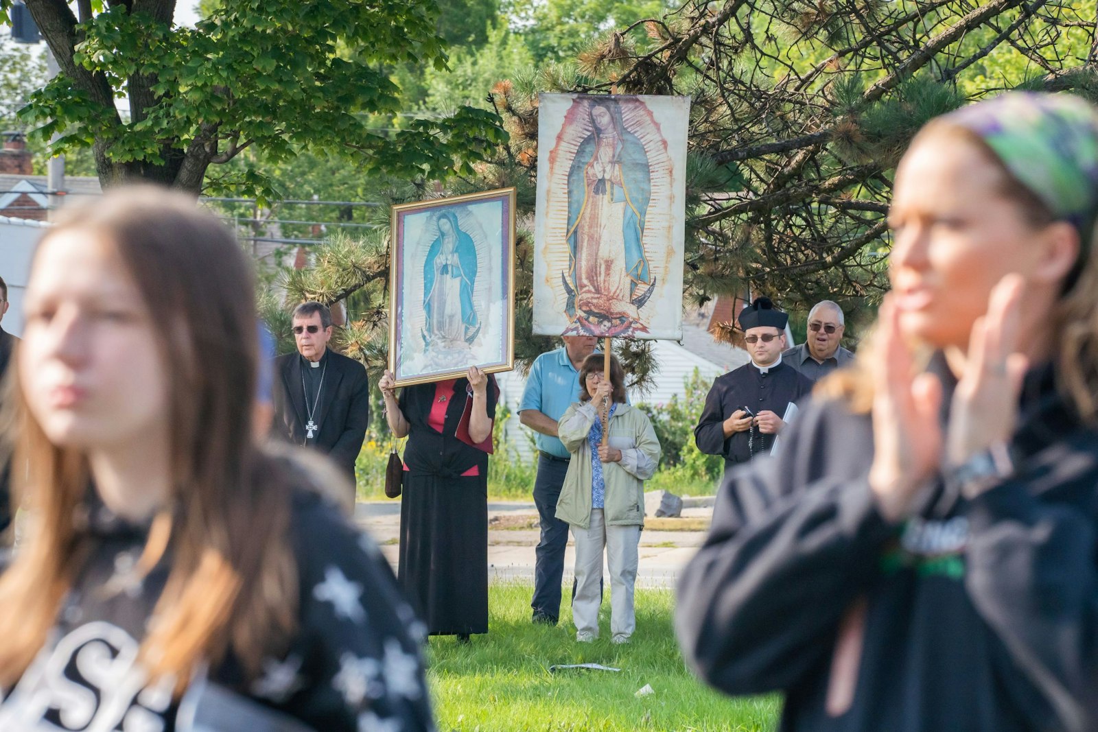 Los jóvenes rezan en primer plano mientras los voluntarios sostienen pancartas de Nuestra Señora de Guadalupe junto al arzobispo Allen H. Vigneron, a la izquierda, y el padre Eric Fedewa durante una vigilia de oración frente a una clínica de abortos en Eastpointe en agosto de 2021. (Valaurian Waller | Detroit Catholic)