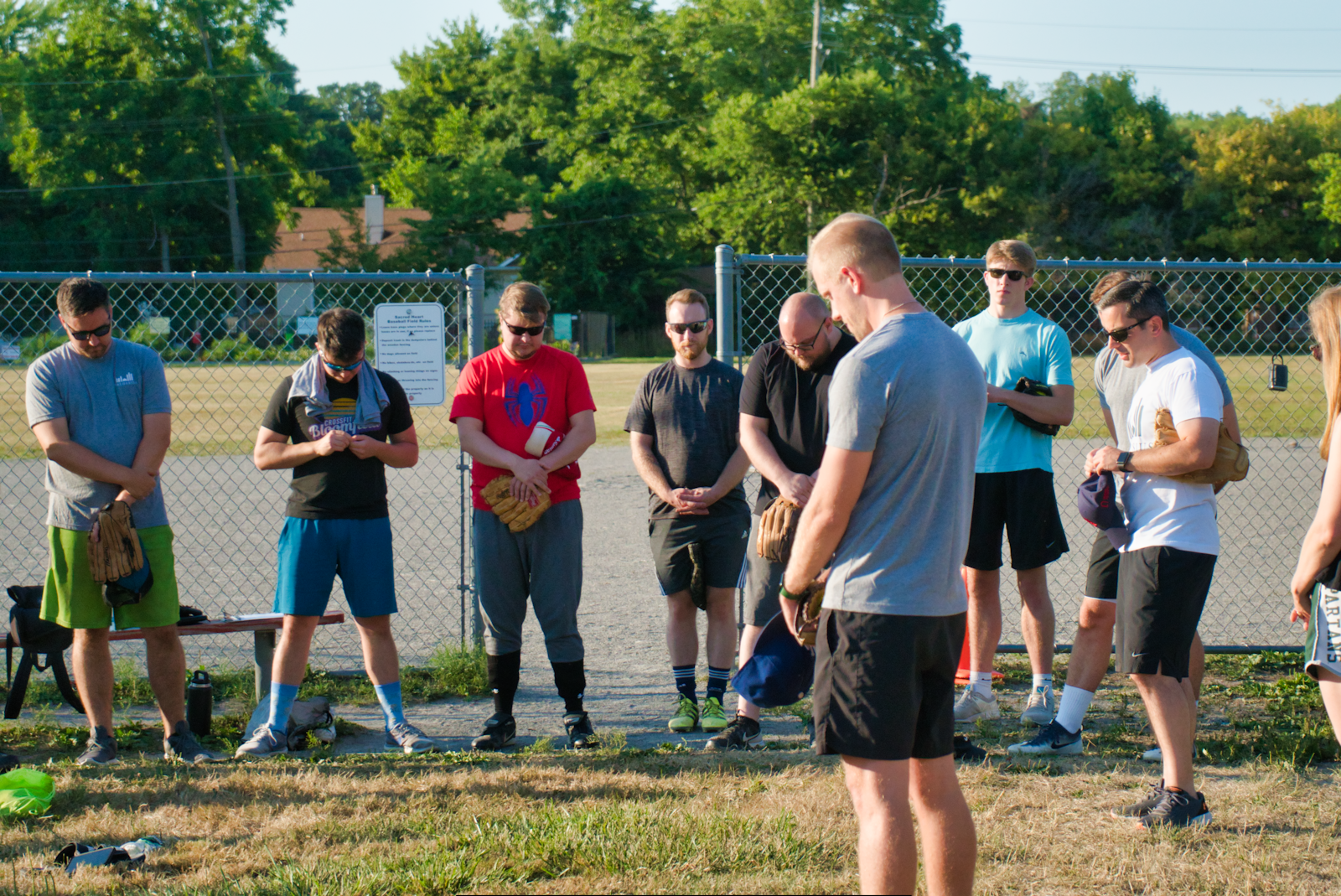 Members of both teams pray before the game Aug. 2 on the softball diamond behind Sacred Heart Parish in Grosse Ile.