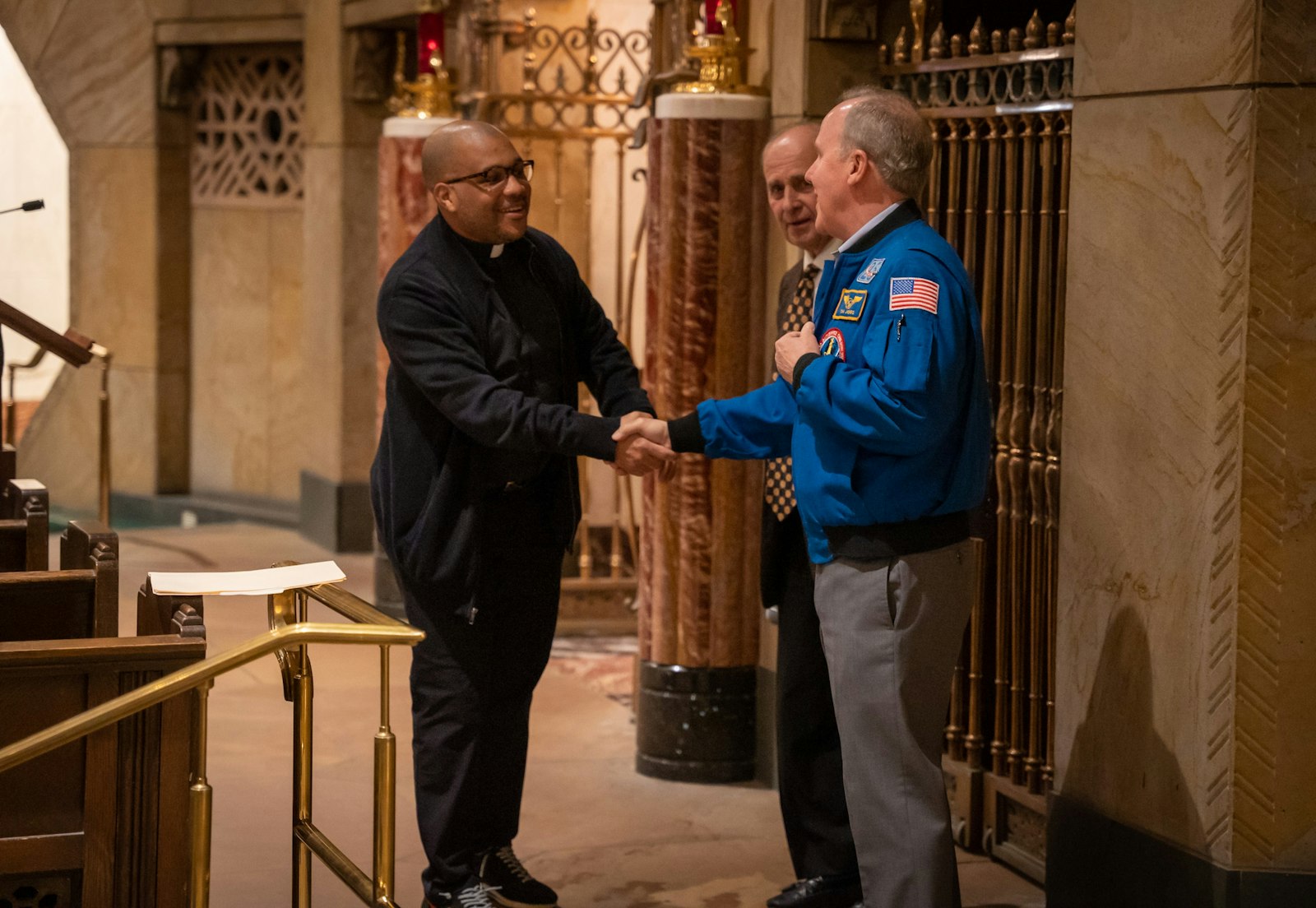 Jones shakes hands with Shrine associate pastor, Fr. John McKenzie, during the “Live at the Basilica” speaker event April 6. Jones spoke how he and two other astronauts were able to take in communion while on mission in outer space, and how much he relied on God in praying for the success and safety of the mission.