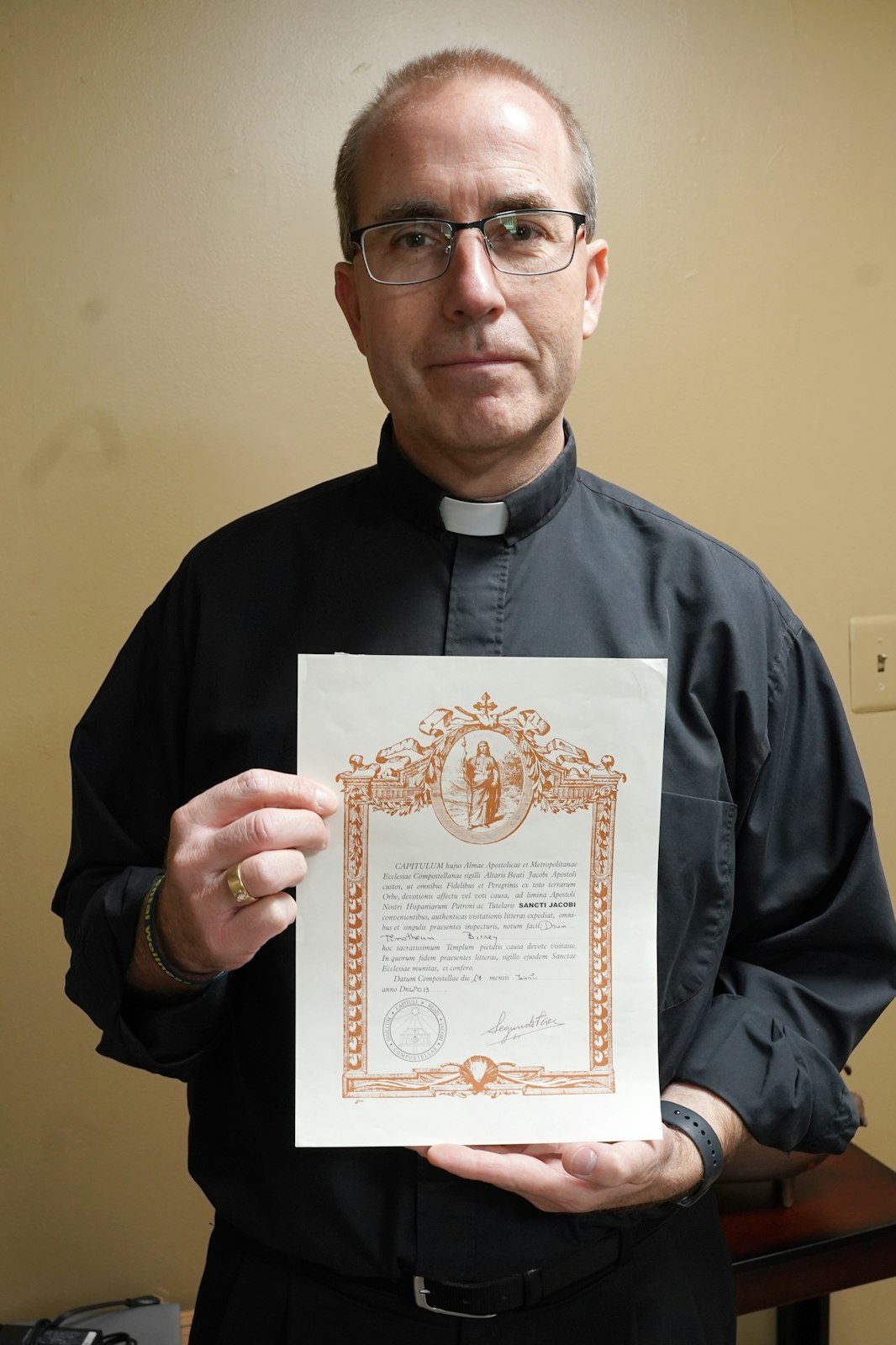 Fr. Tim Birney holds up his El Camino Compostela for completing the Camino de Santiago. After each Camino, the pilgrims gets to determine if they made the journey for spiritual or recreational reasons. Fr. Birney estimates its about  50-50 split between the two. (Photo by Daniel Meloy | Detroit Catholic)