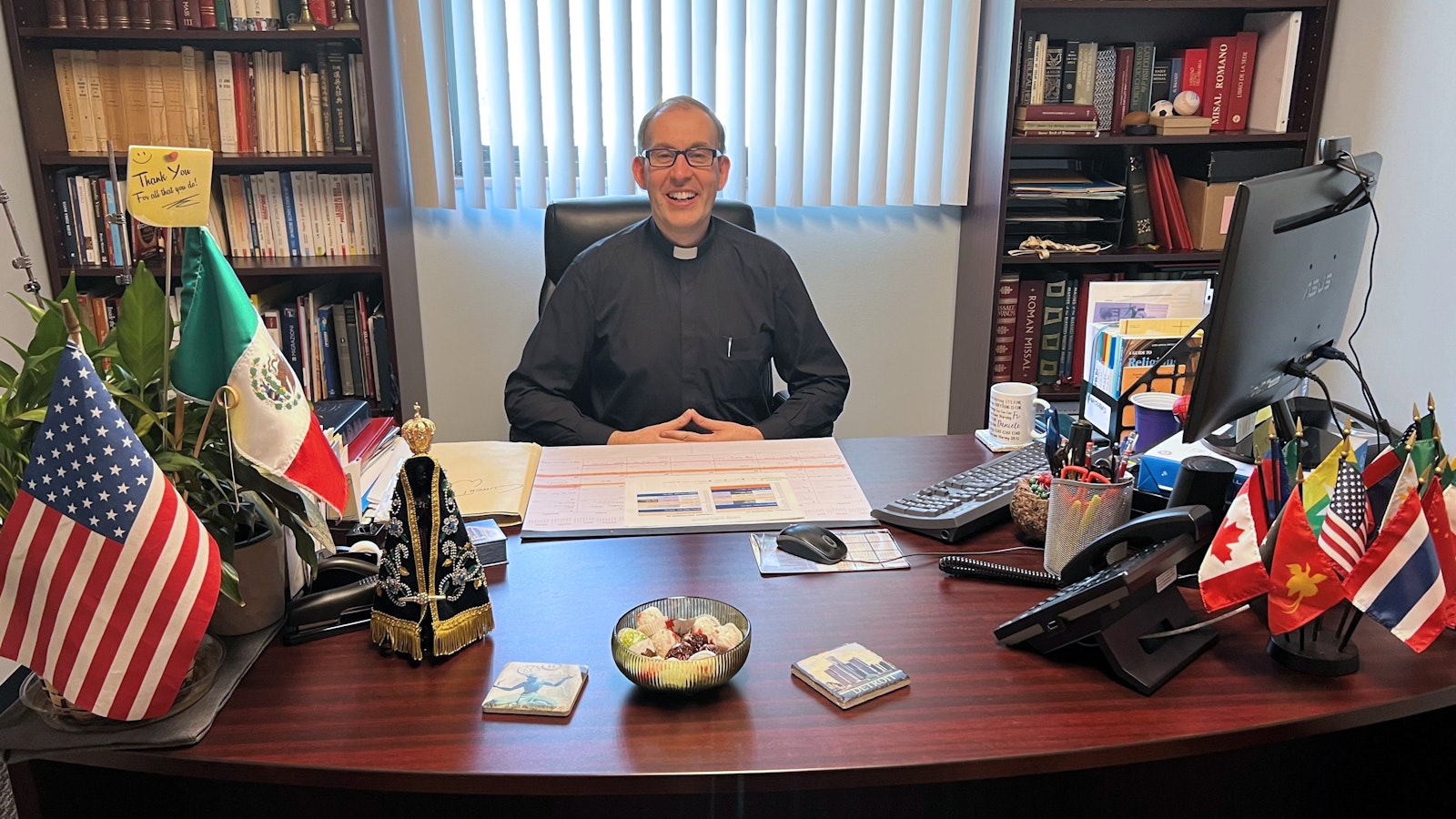 Surrounded by flags of the various countries in which PIME Missionaries serve, Fr. Daniele Criscione smiles behind his desk in the new PIME U.S. Mission Center headquarters.