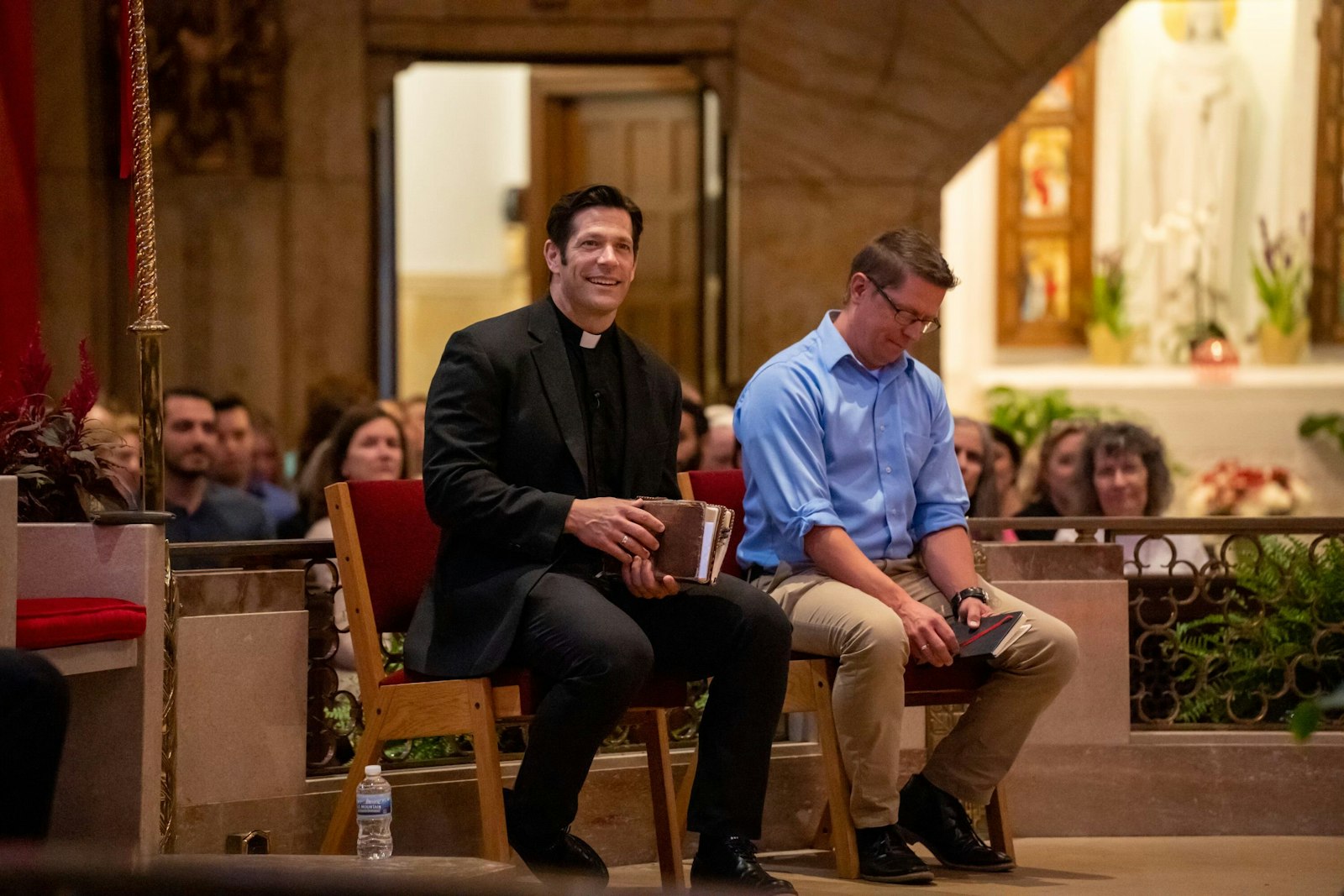 El padre Schmitz sonríe mientras se prepara para hablar durante el evento "Live at the Basilica" junto a Nick Davidson. La serie de oradores trae a conocidos oradores católicos de todo el país para una charla mensual en la basílica de Royal Oak. (Valaurian Waller | Detroit Catholic)