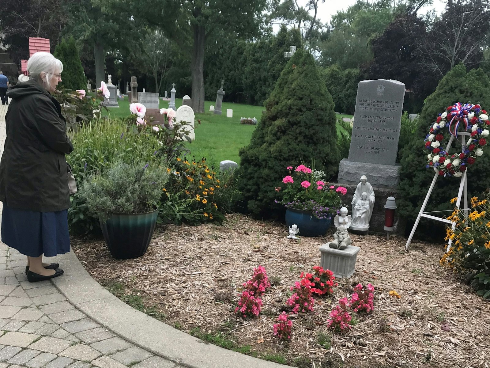 A woman prays near the grave marker for aborted children in Assumption Grotto's cemetery in northwest Detroit during the memorial service Sept. 9. (Kelly Luttinen | Special to Detroit Catholic)