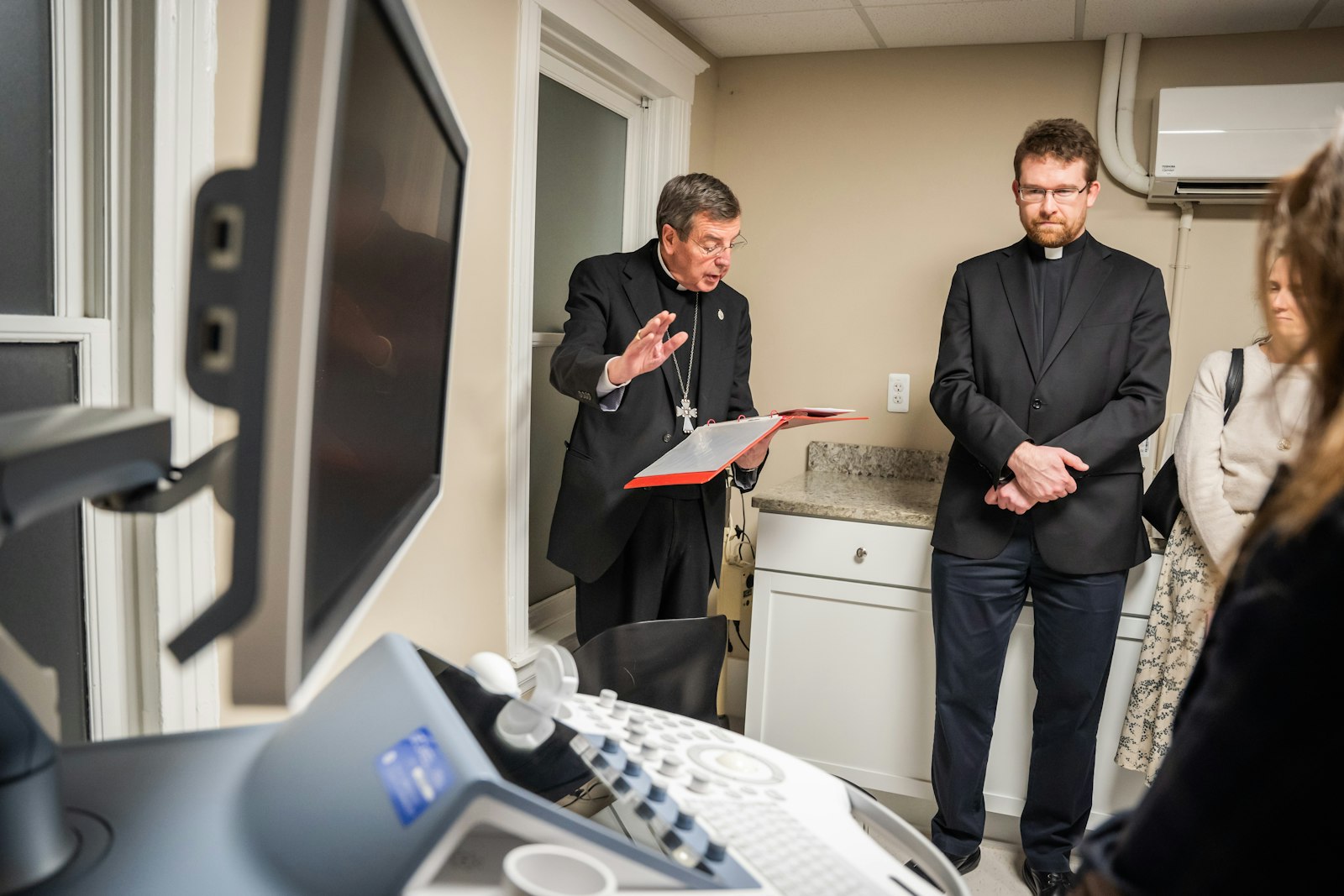 Archbishop Vigneron blesses the clinic's new ultrasound machine donated by Knights of Columbus Council 2950 from St. Lawrence Parish in Utica.