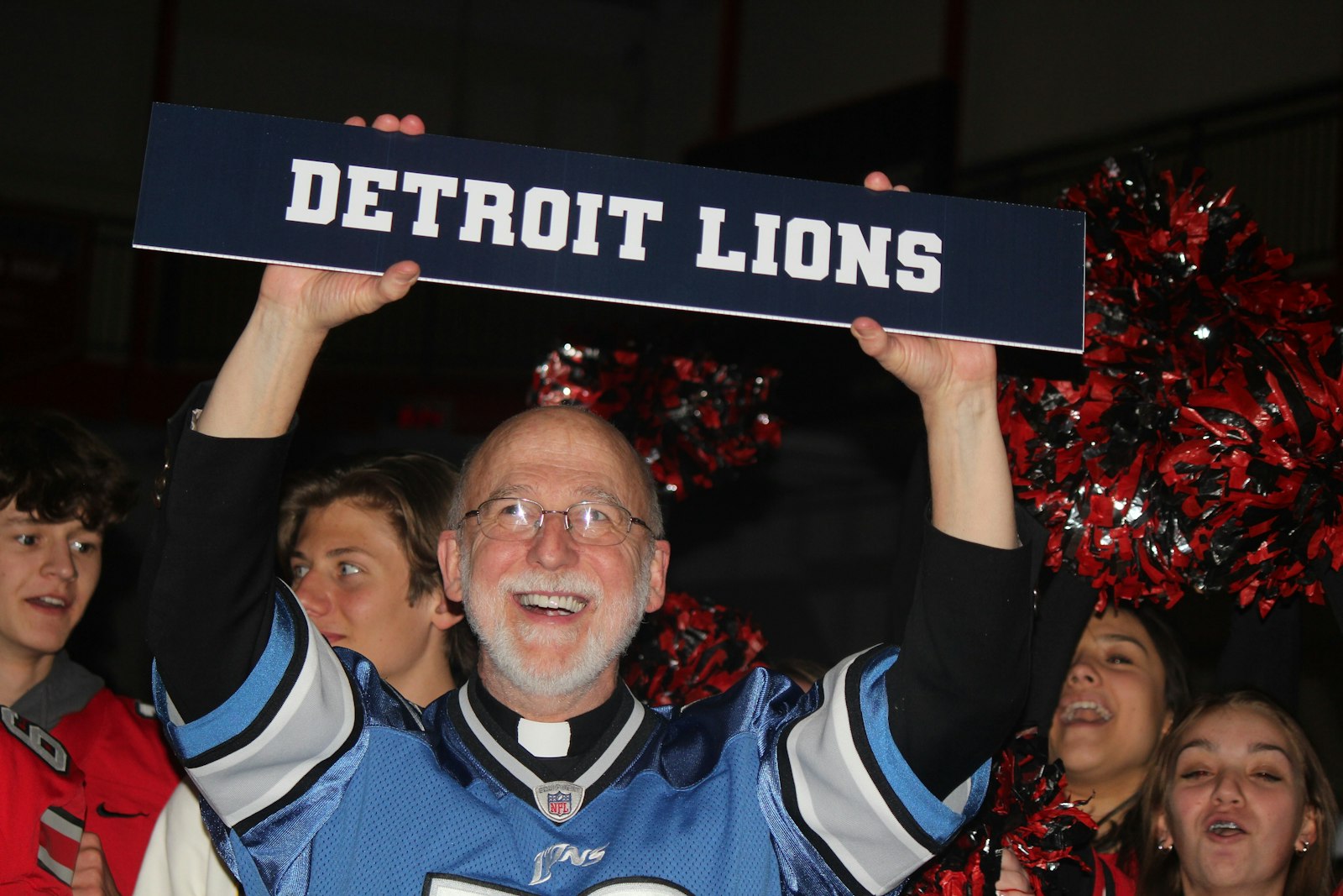 Divine Child pastor Fr. Bob McCabe brings out the Detroit Lions sign to attach to Aidan Hutchinson’s standee after he is announced as the Lions’ first draft pick.