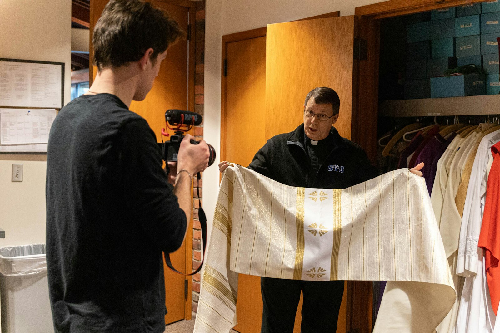 Fr. Kean explains some of the priestly vestments he wears as Sasak films in the sacristy of St. Joseph the Worker Parish in Lake Orion.