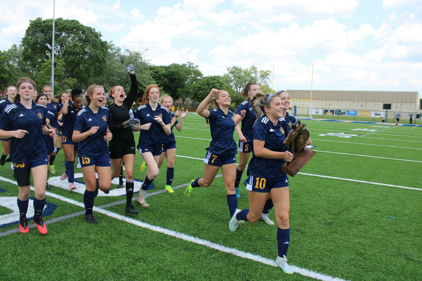 After defeating Plymouth Christian 2-0 to win the regional crown, Royal Oak Shrine soccer players rush toward the fan section with the championship trophy in hand.
