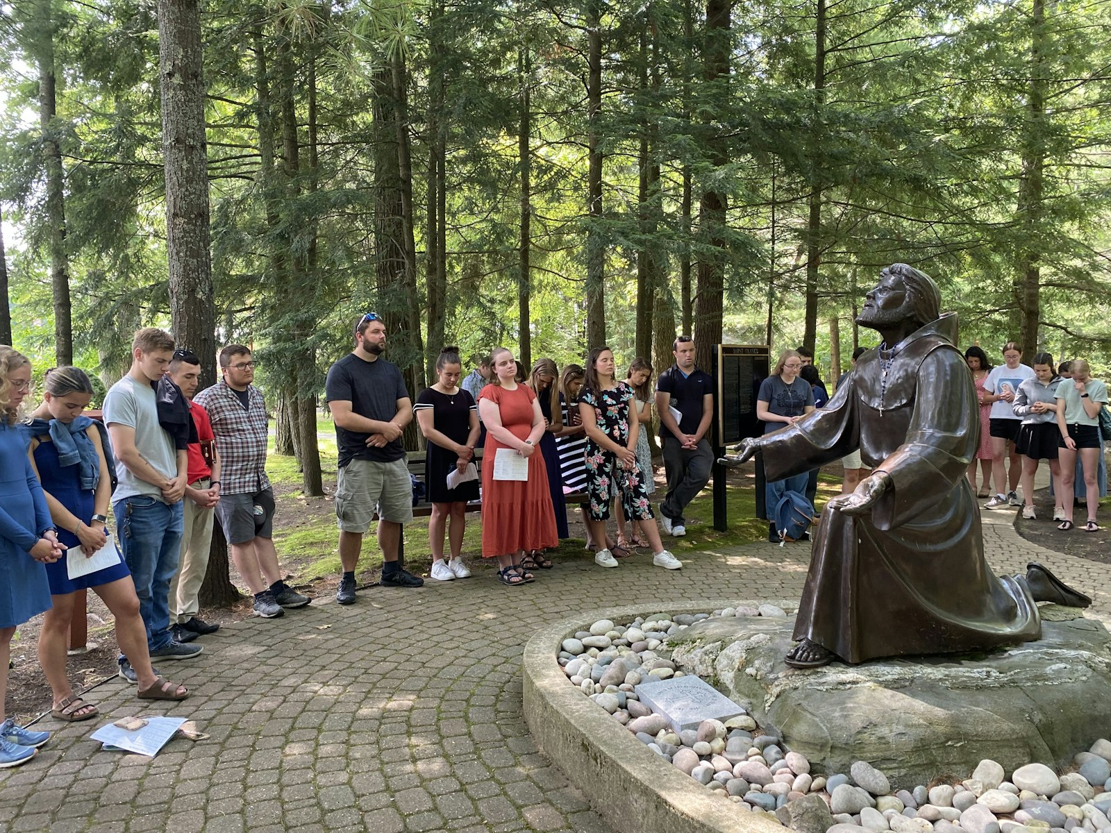 Young adults gather around a statue of St. Francis of Assisi for the final meeting of the 2023 Michigan Young Adult Hiking and Rafting Pilgrimage. The theme of the pilgrimage was finding God's peace.