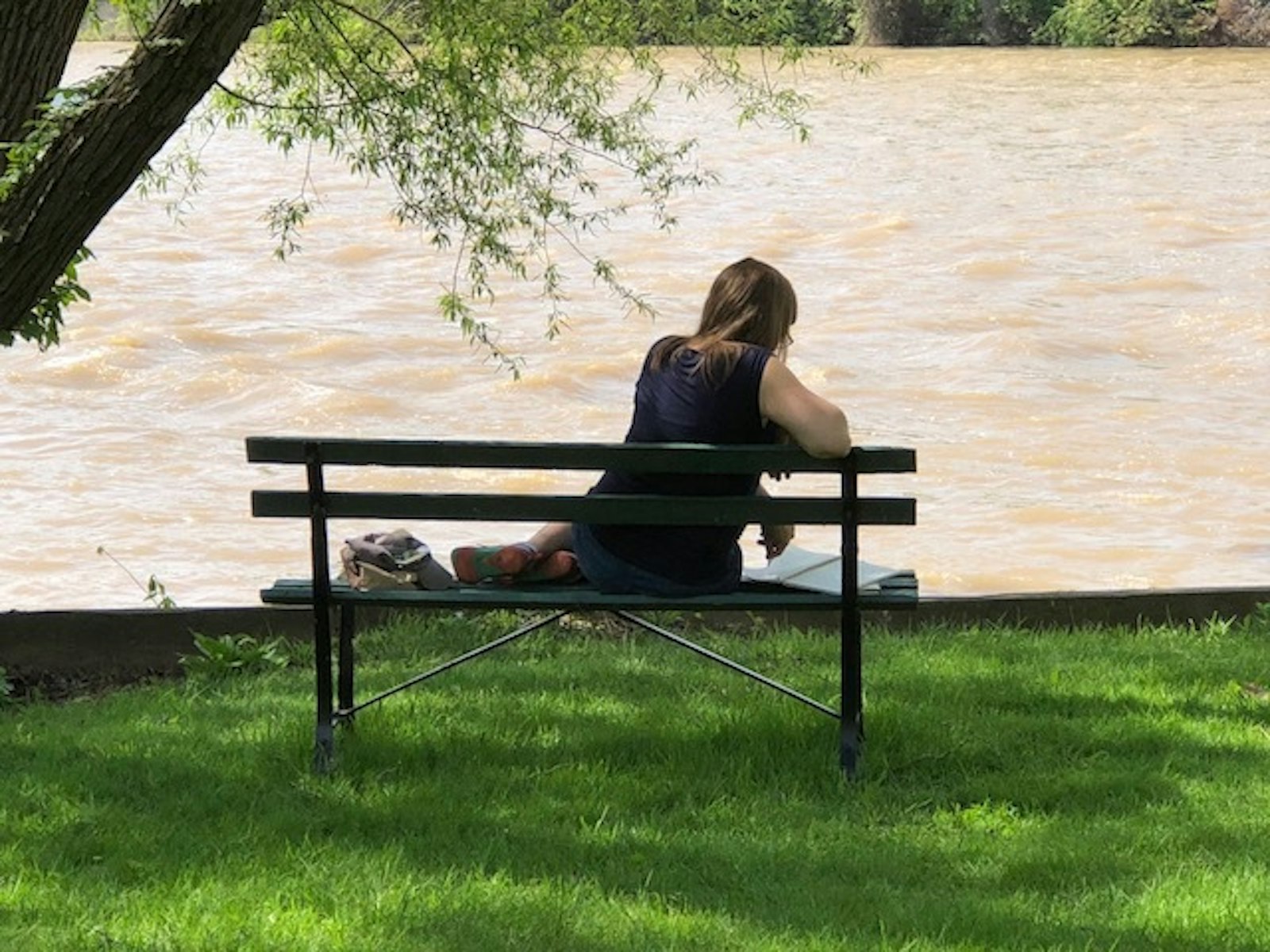 Una mujer se sienta en un banco con vista al río Raisin en IHM River House en Monroe durante los meses de verano. (Foto de cortesía)