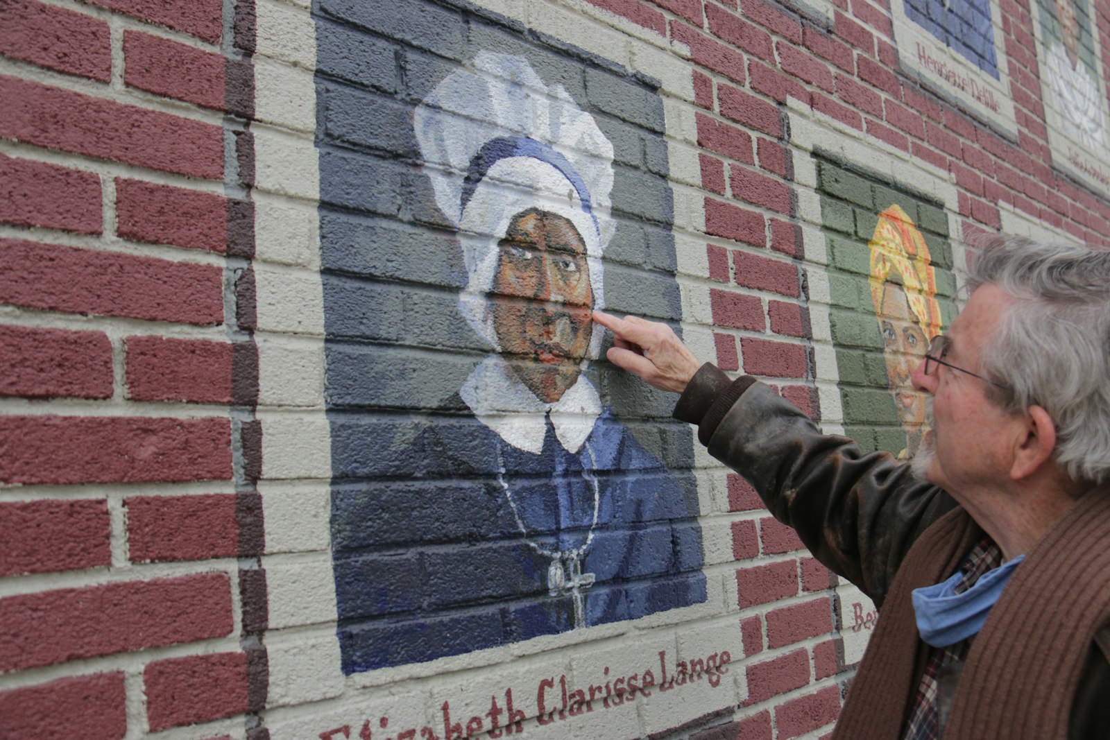 Orlowski points out details on his portrait of Mother Mary Lange, painted onto the brick façade of the Center for the Works of Mercy in Detroit.