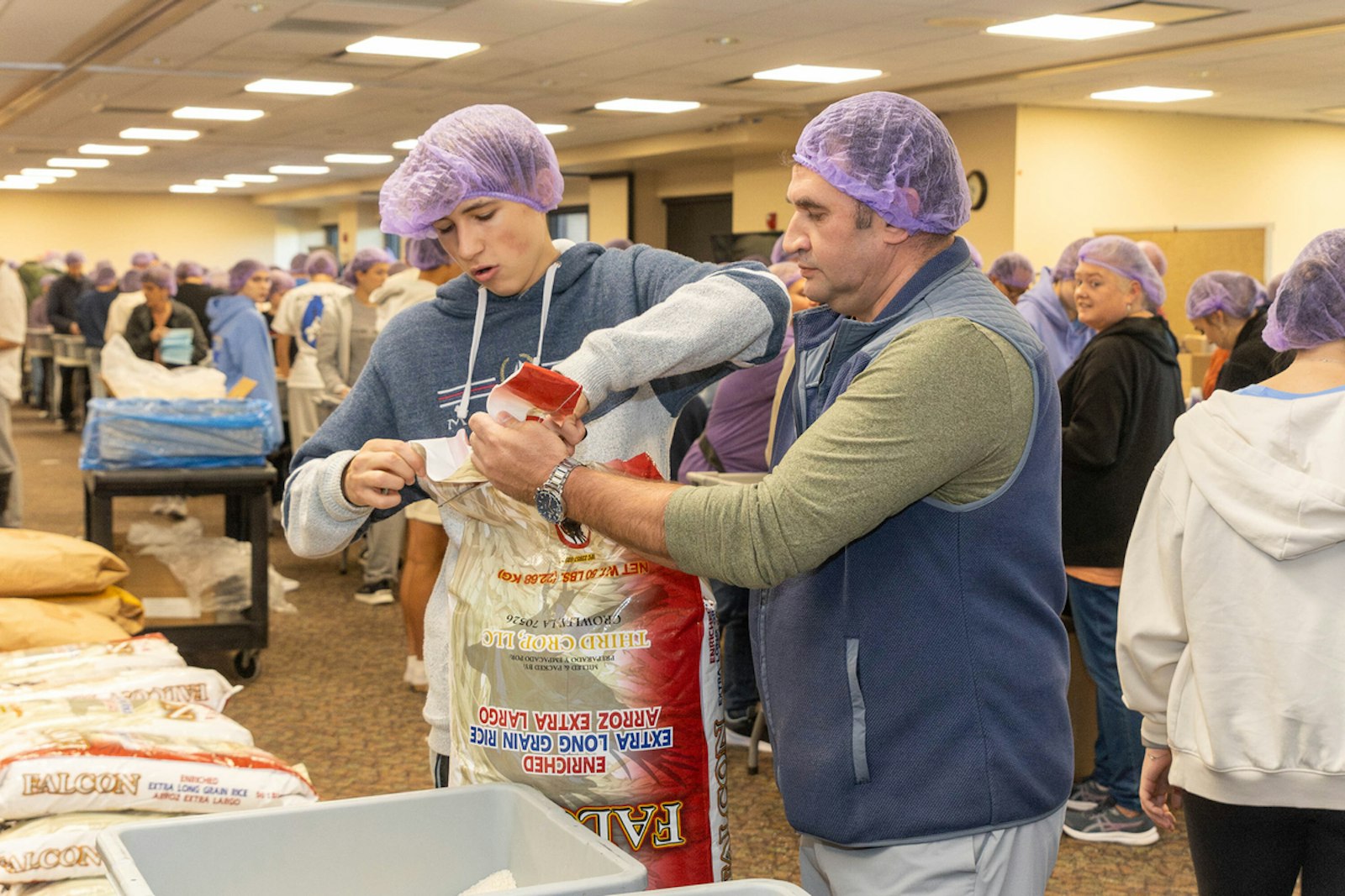 Volunteers cut open new bags of rice to refill packaging stations at St. Isidore. The entire effort took just over two hours to pack 100,000 meals in an assembly-line format.