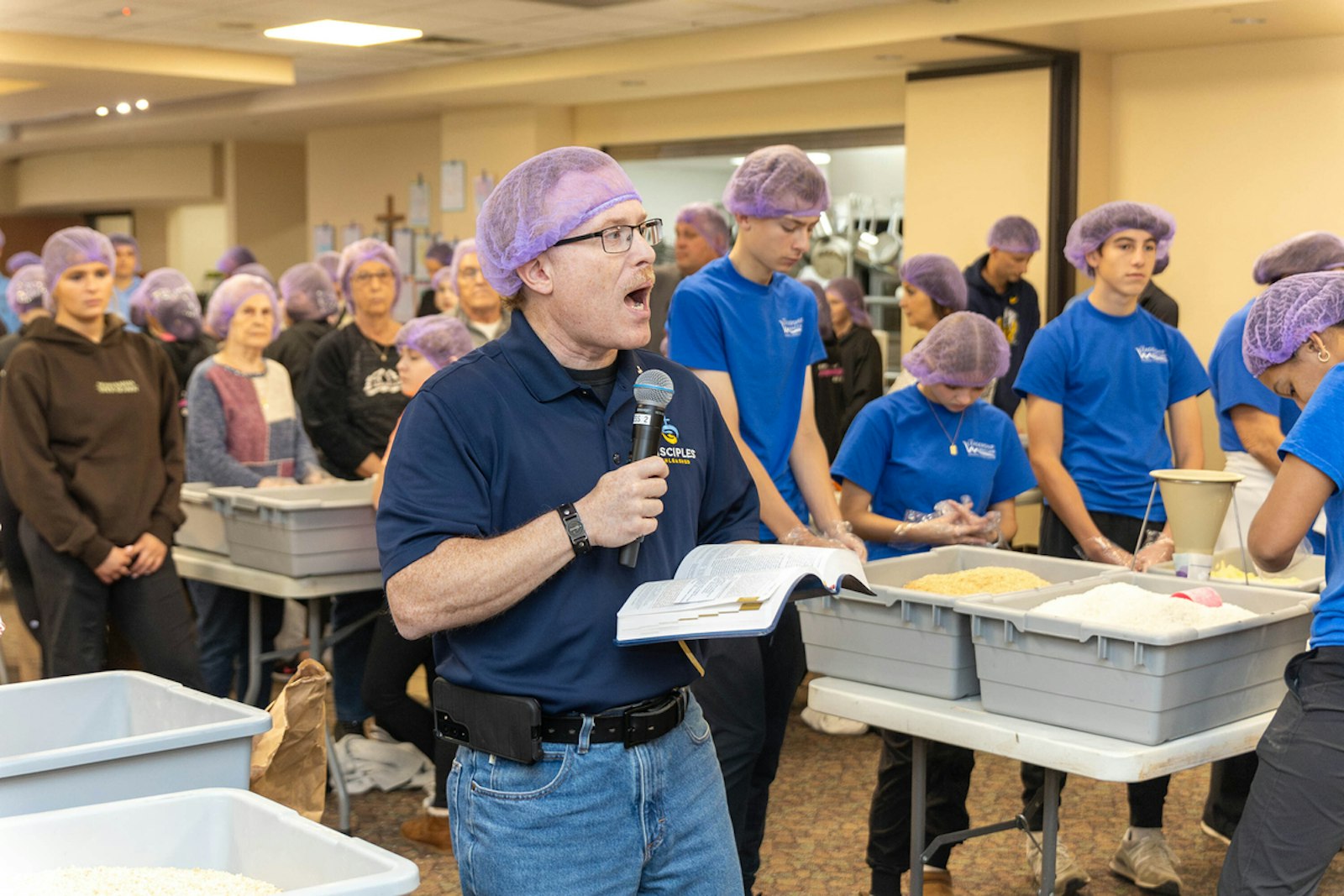 Deacon Jeffrey Loeb of St. Isidore Parish reads a passage from Scripture as volunteers pause to pray during a massive food packaging operation Nov. 2 at the Macomb church.