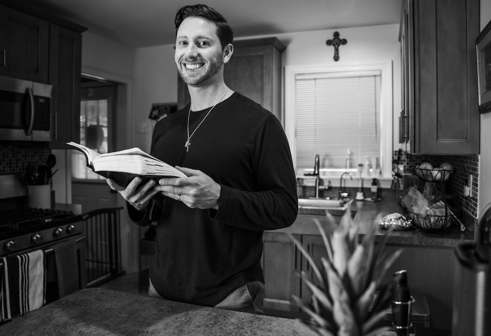 Jordan Beachnau smiles in his home while holding the Bible during a photo shoot. Beachnau was one of hundreds who shared his story of Eucharistic devotion via the I AM HERE campaign.