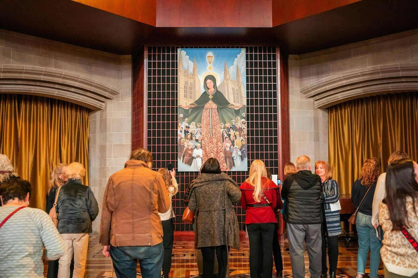 Varios fieles contemplan un nuevo cuadro del artista Christopher Darga, titulado "María, Madre de la Iglesia de Detroit". El cuadro representa a la Virgen rodeada de algunos de los mayores santos de la Iglesia.